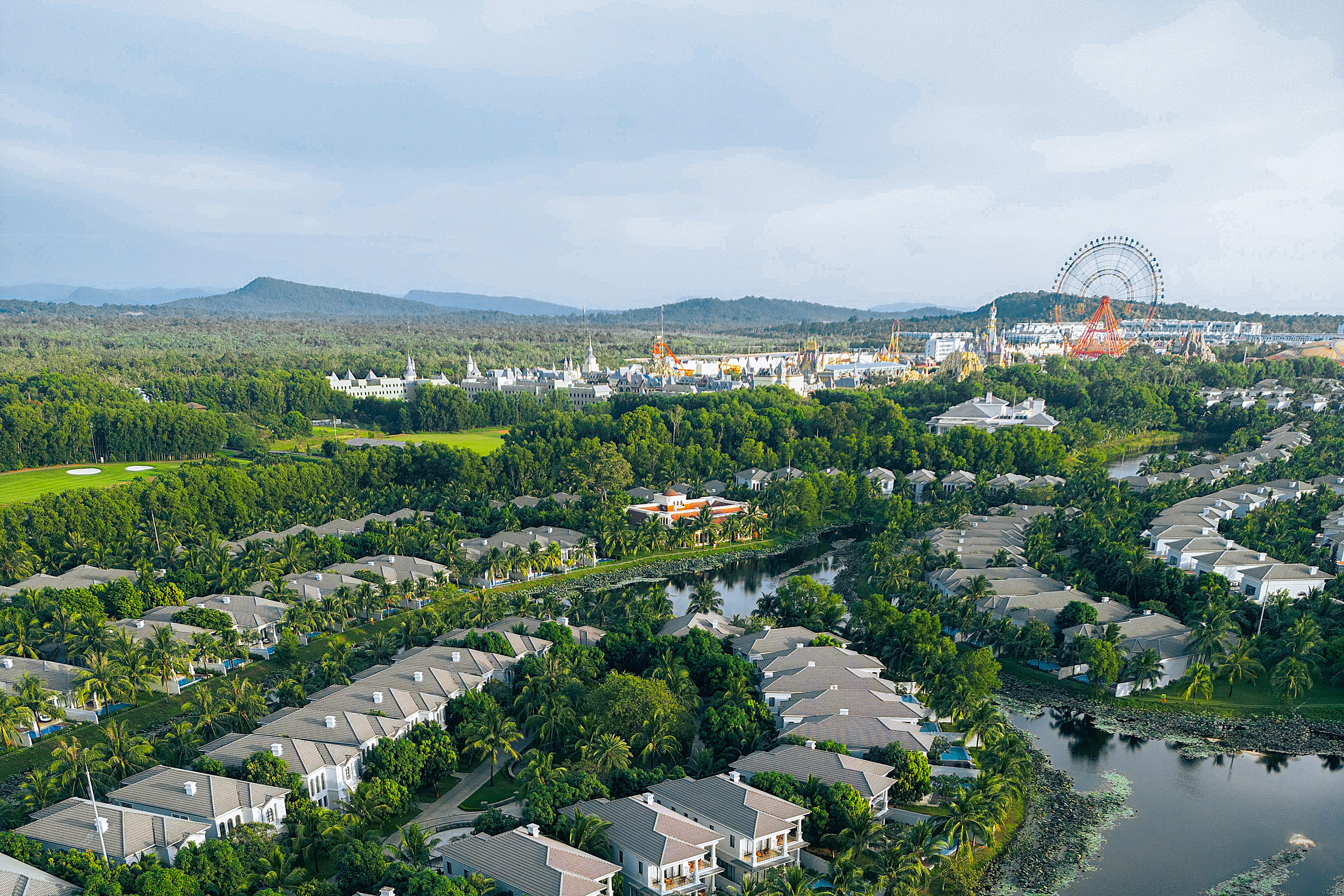 Aerial tropical resort, luxury villas, golf course, lake, theme park Ferris wheel.