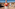 Smiling woman in orange top and white shorts hiking desert trail with man.