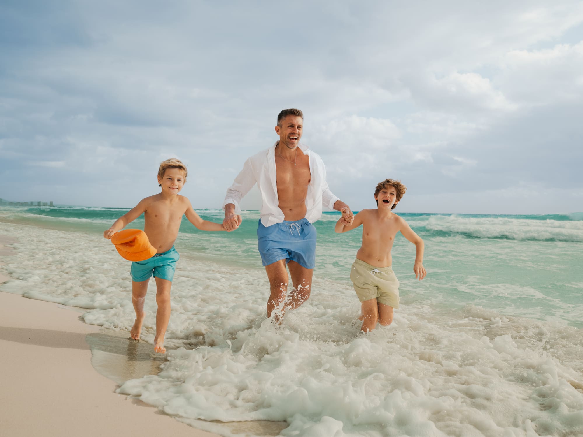 Family beach fun: father and two sons running in ocean waves.