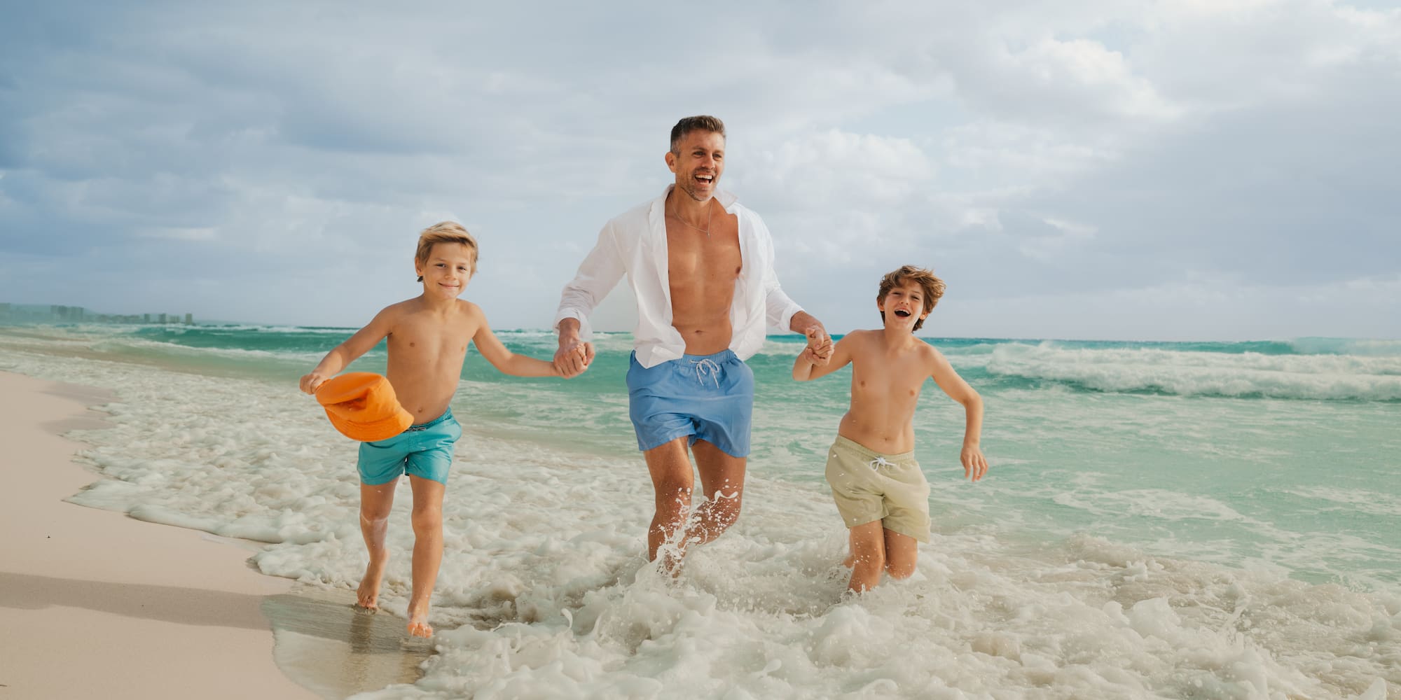 Family beach fun: father and two sons running in ocean waves.