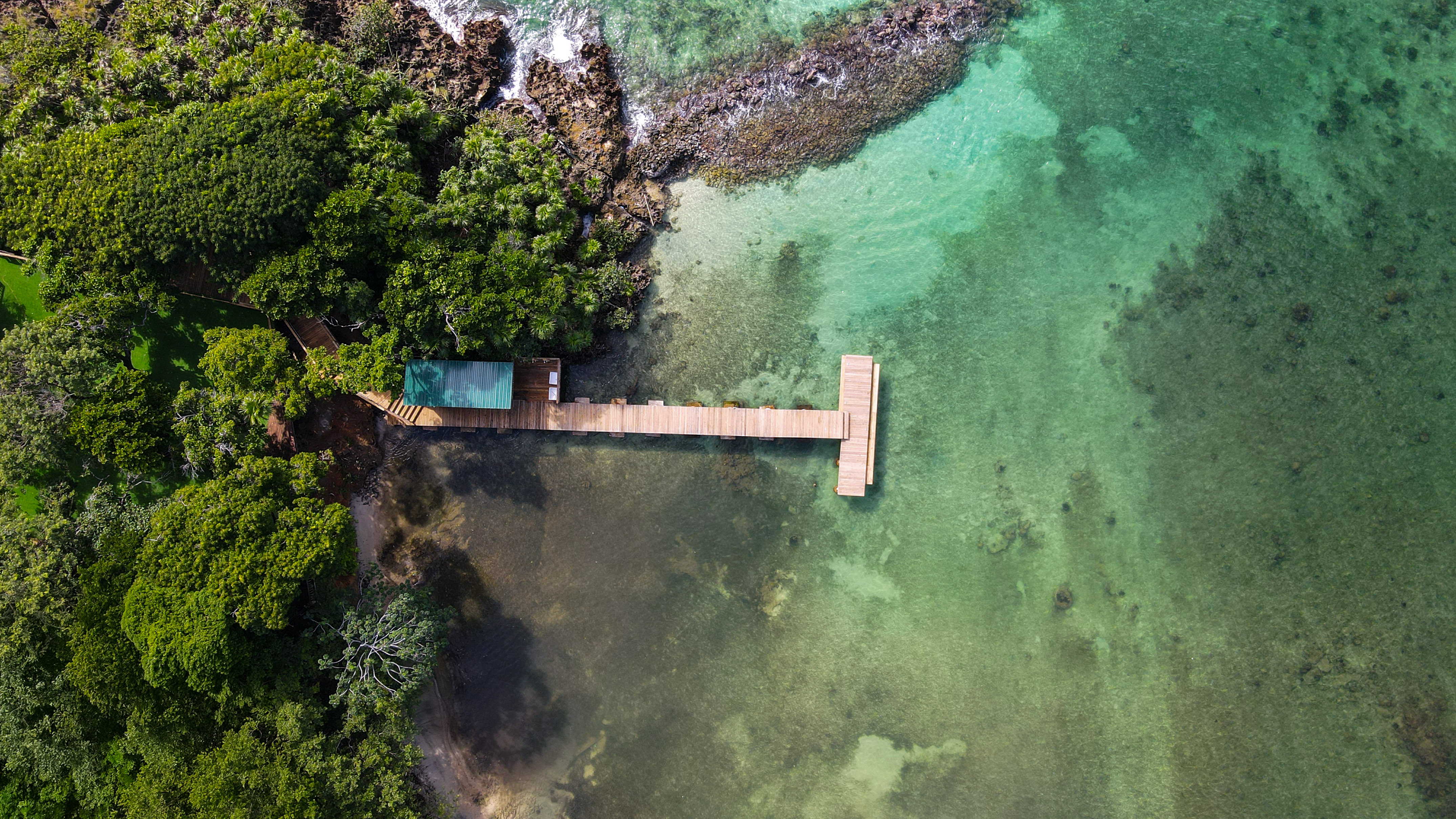 Aerial view of tropical pier over clear turquoise water and lush green forest.