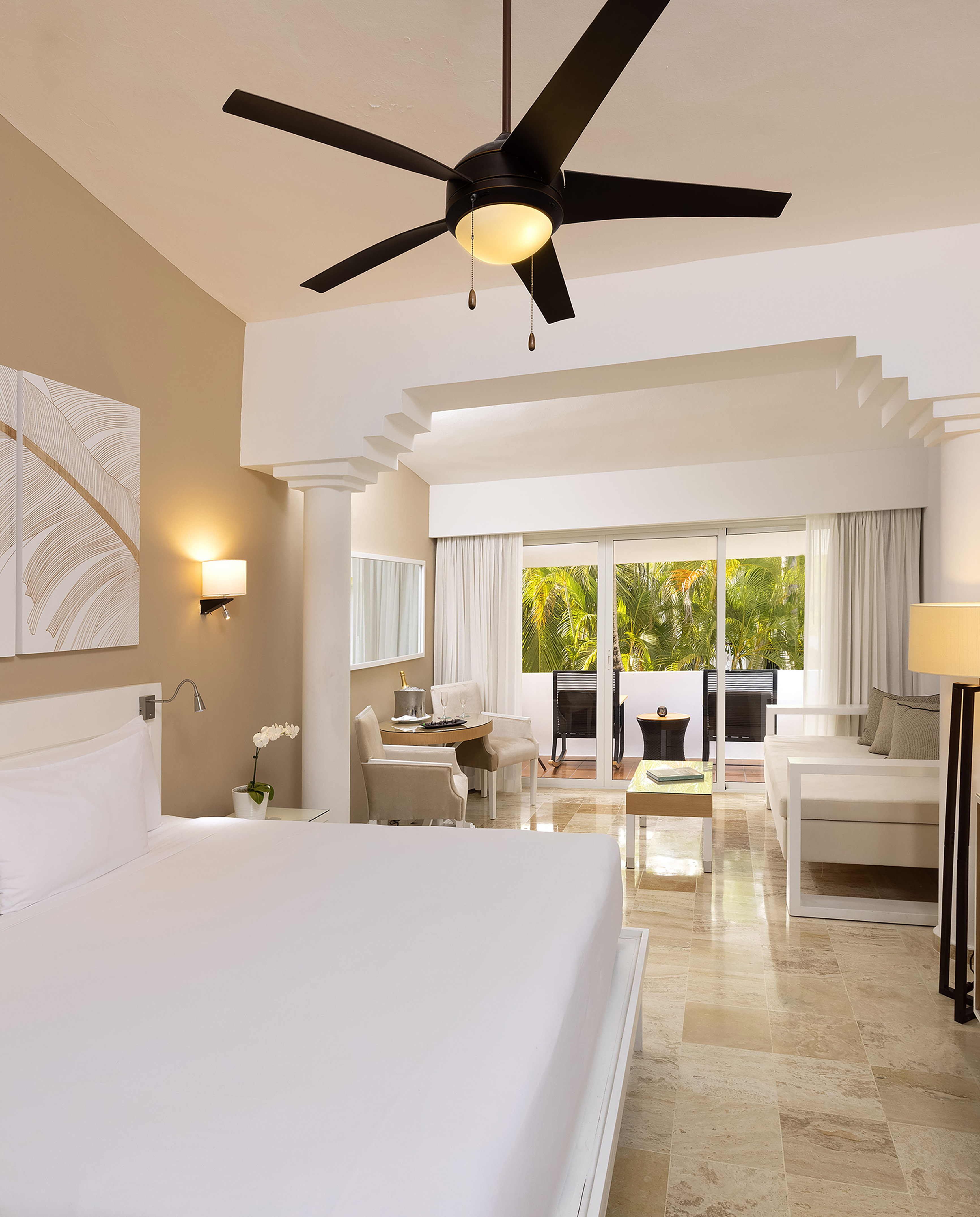 Luxury hotel suite with king bed, seating area, and tropical balcony view.