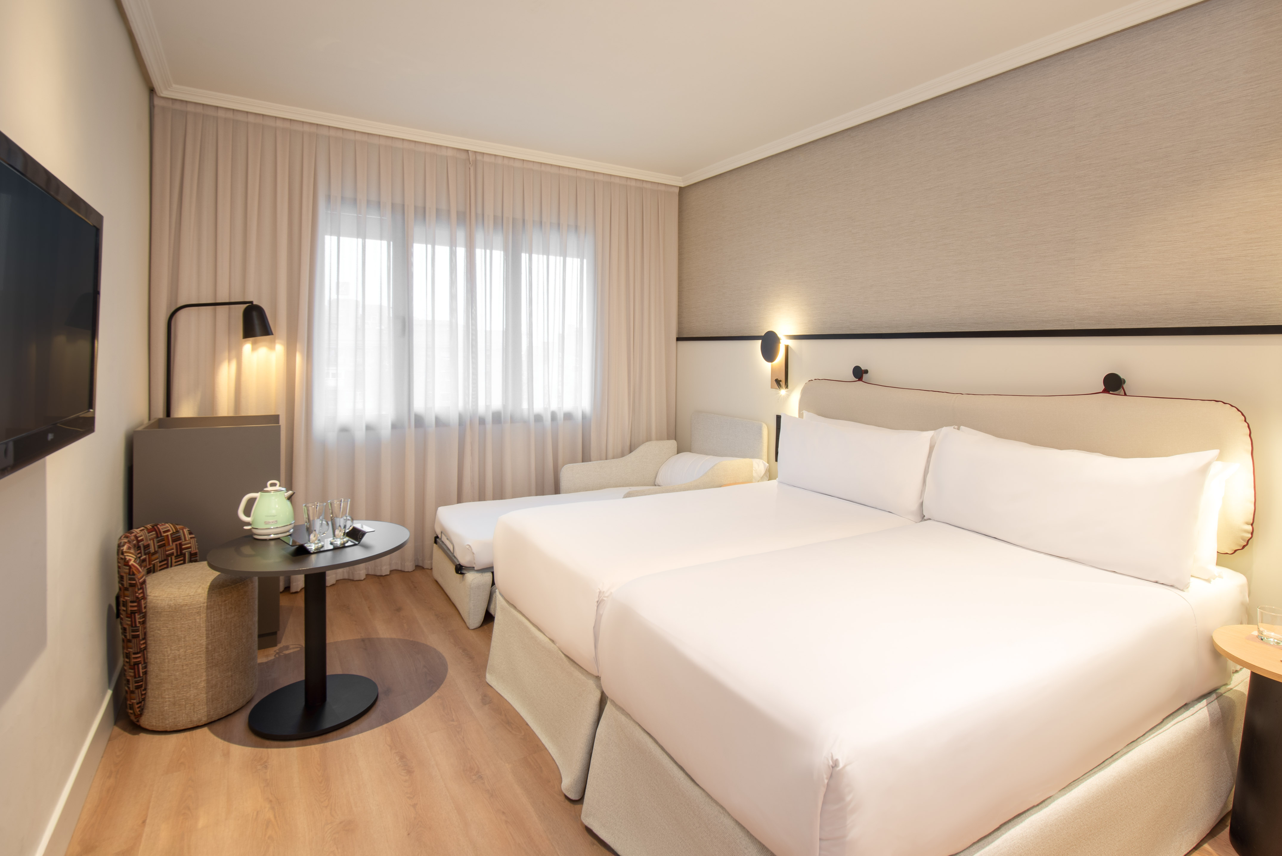 Modern hotel room with twin beds, sofa bed, TV, and kettle.