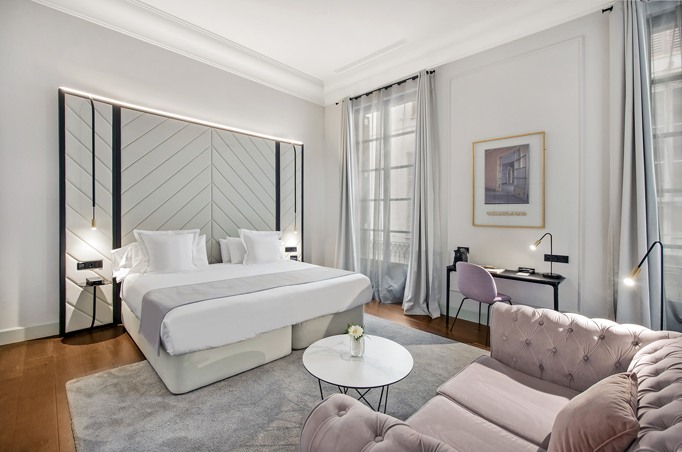 Modern luxury hotel room with king bed, pink sofa, and workspace.