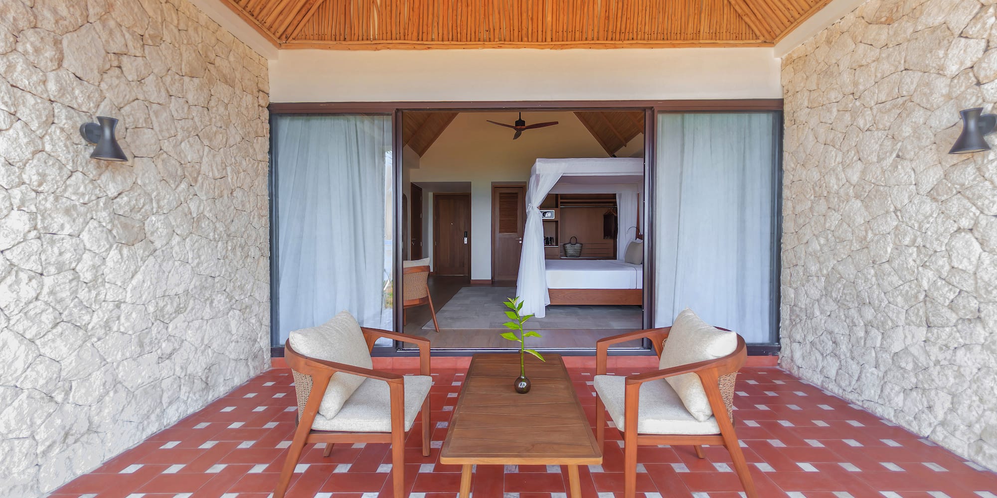Tropical resort patio leading to a bedroom with canopy bed and red tiled floor.