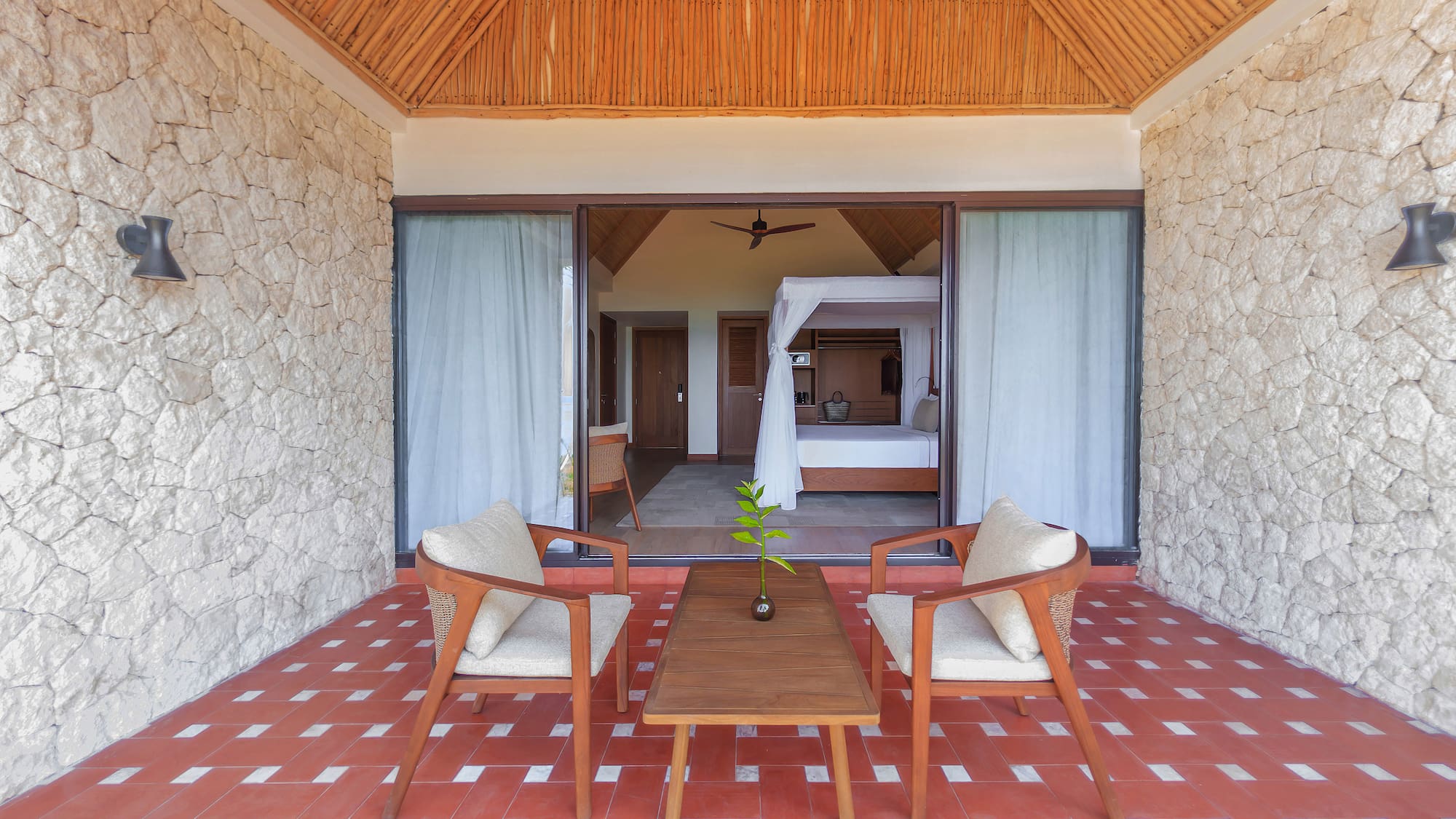 Tropical resort patio leading to a bedroom with canopy bed and red tiled floor.