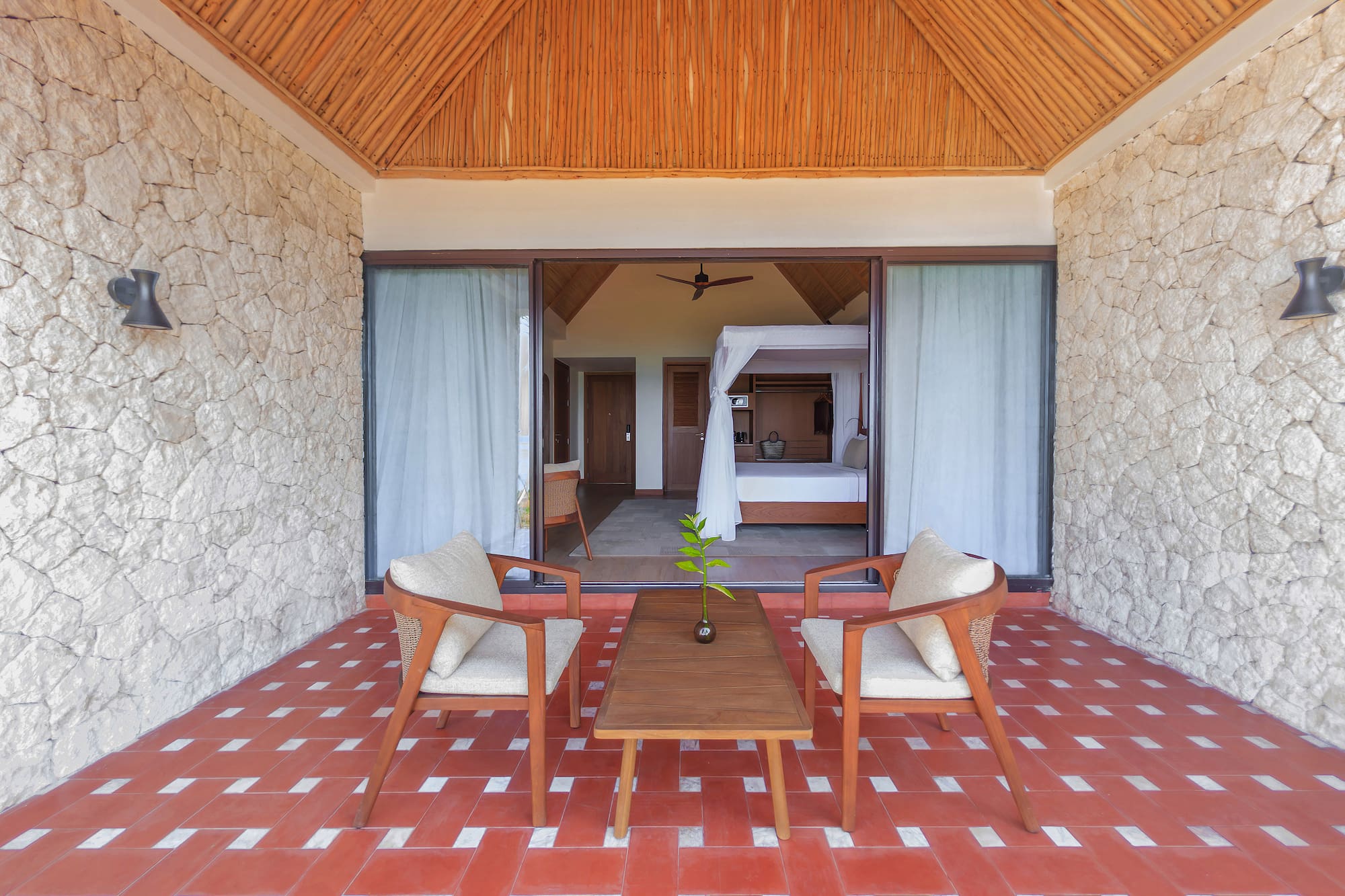 Tropical resort patio leading to a bedroom with canopy bed and red tiled floor.