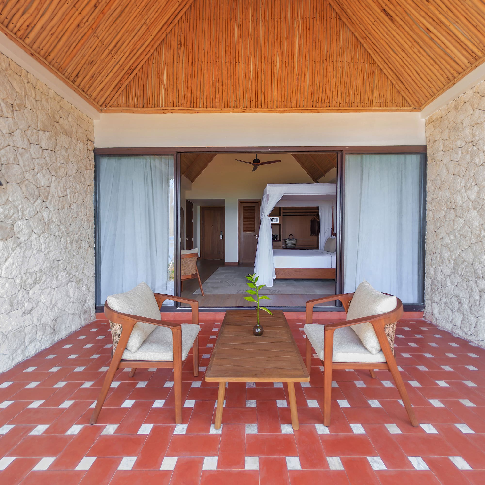 Tropical resort patio leading to a bedroom with canopy bed and red tiled floor.