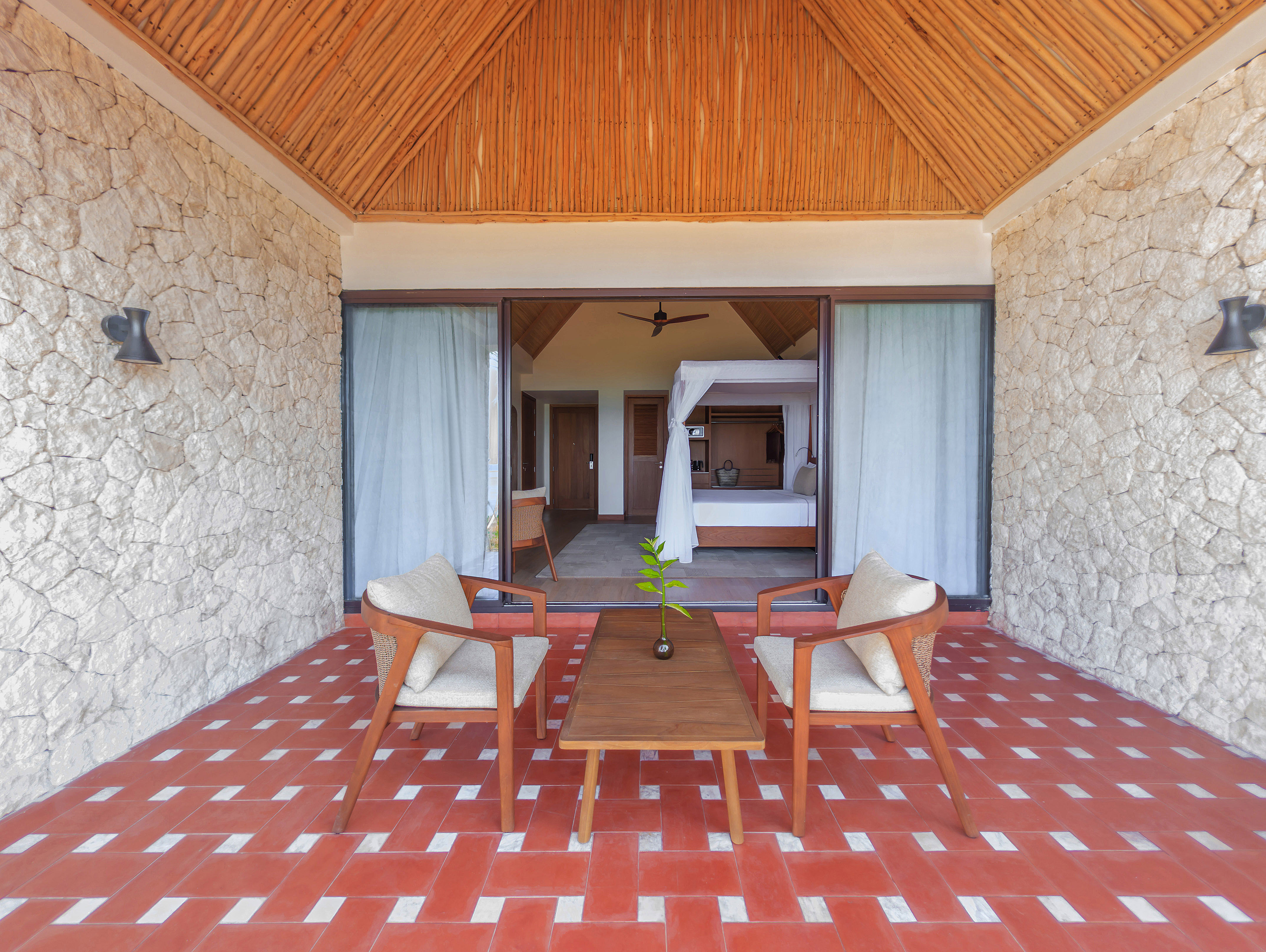 Tropical resort patio leading to a bedroom with canopy bed and red tiled floor.