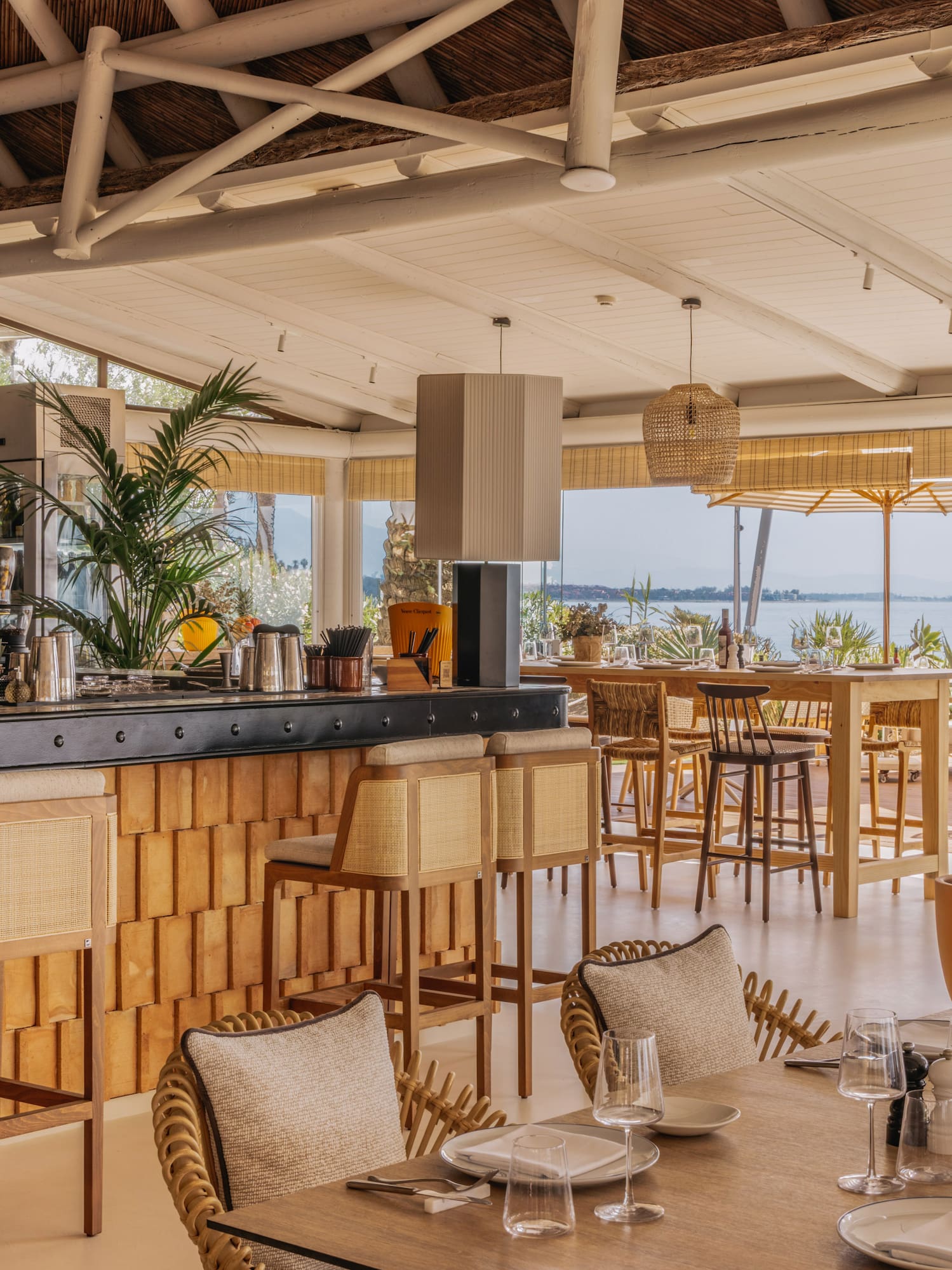 Luxury waterfront restaurant bar with natural wood, rattan, and ocean views.