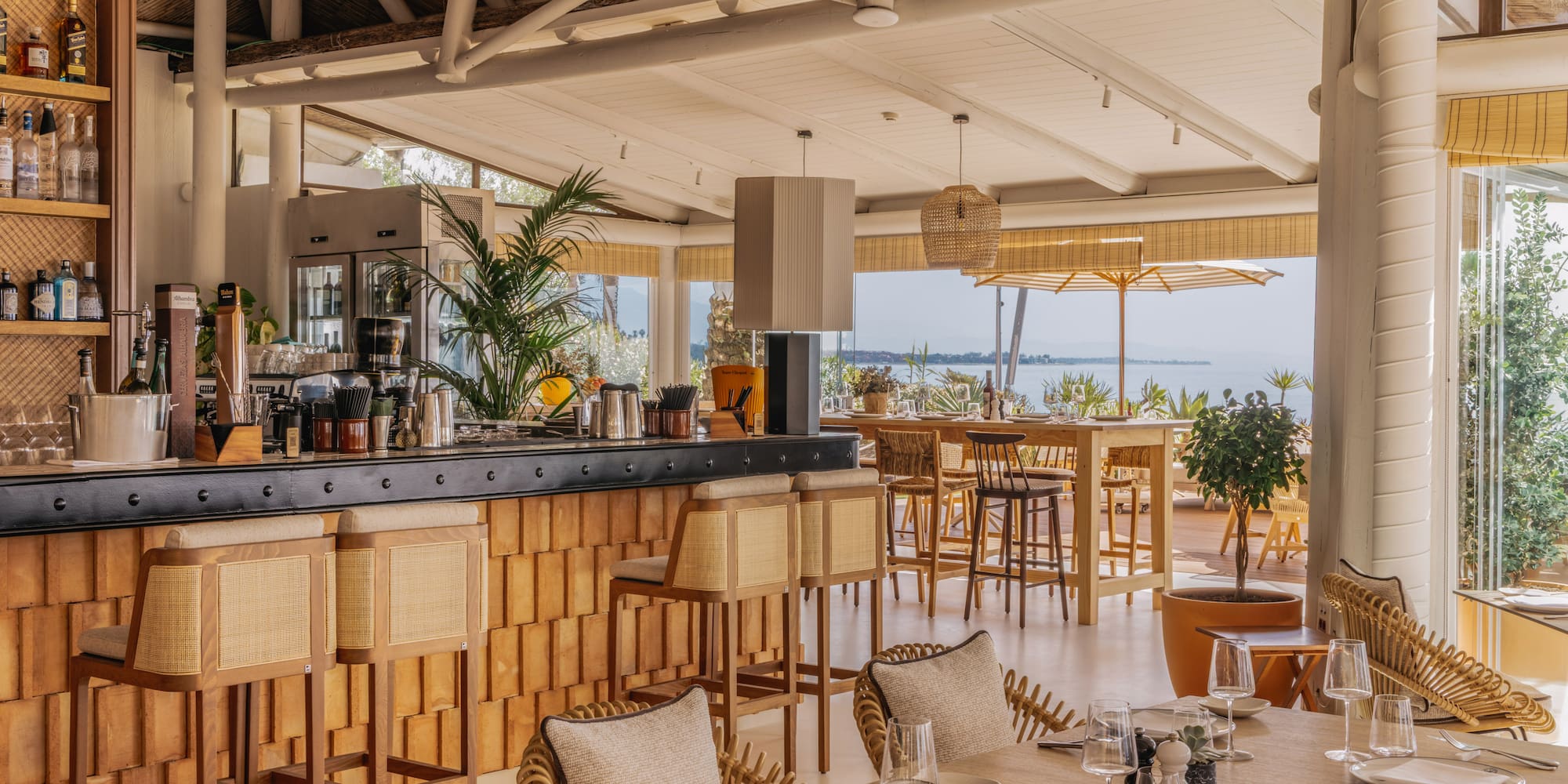 Coastal restaurant bar with rattan furniture, ocean view, and elegant dining.