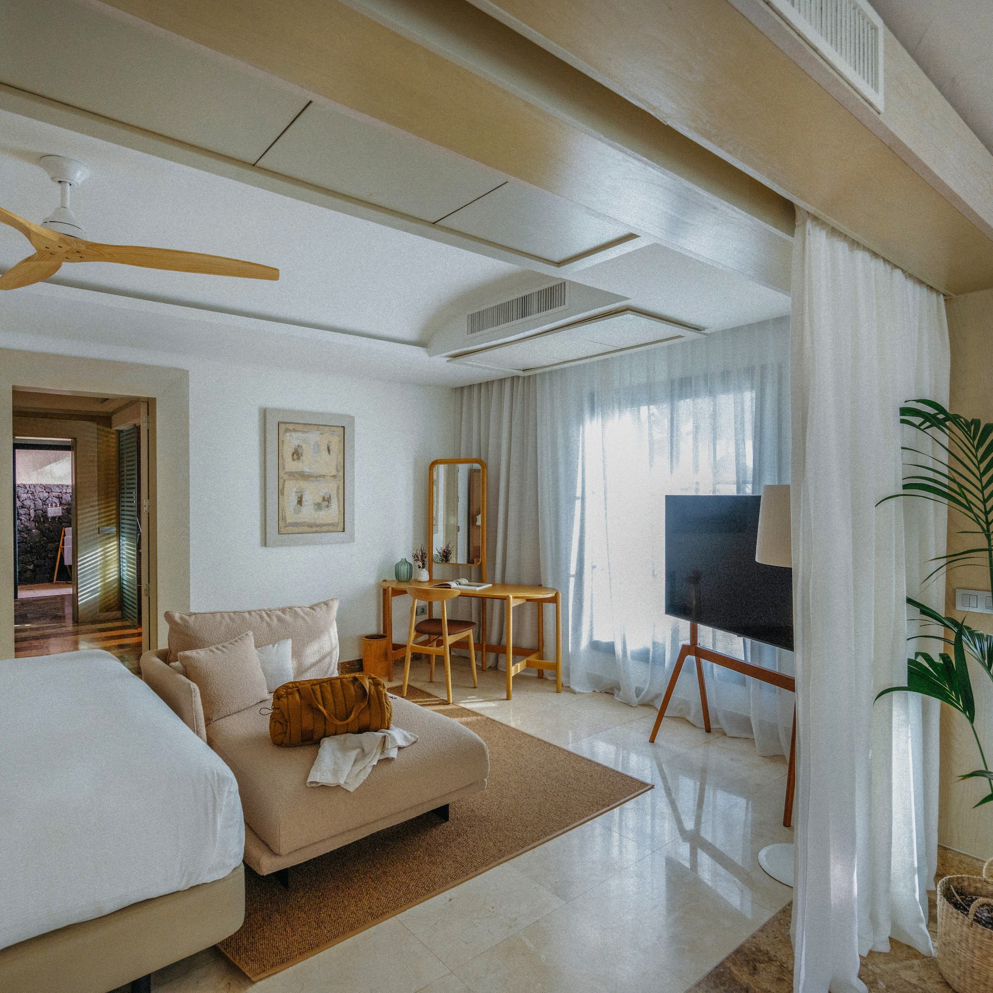 Modern bedroom with chaise lounge, wood desk, ceiling fan, and outdoor pool.