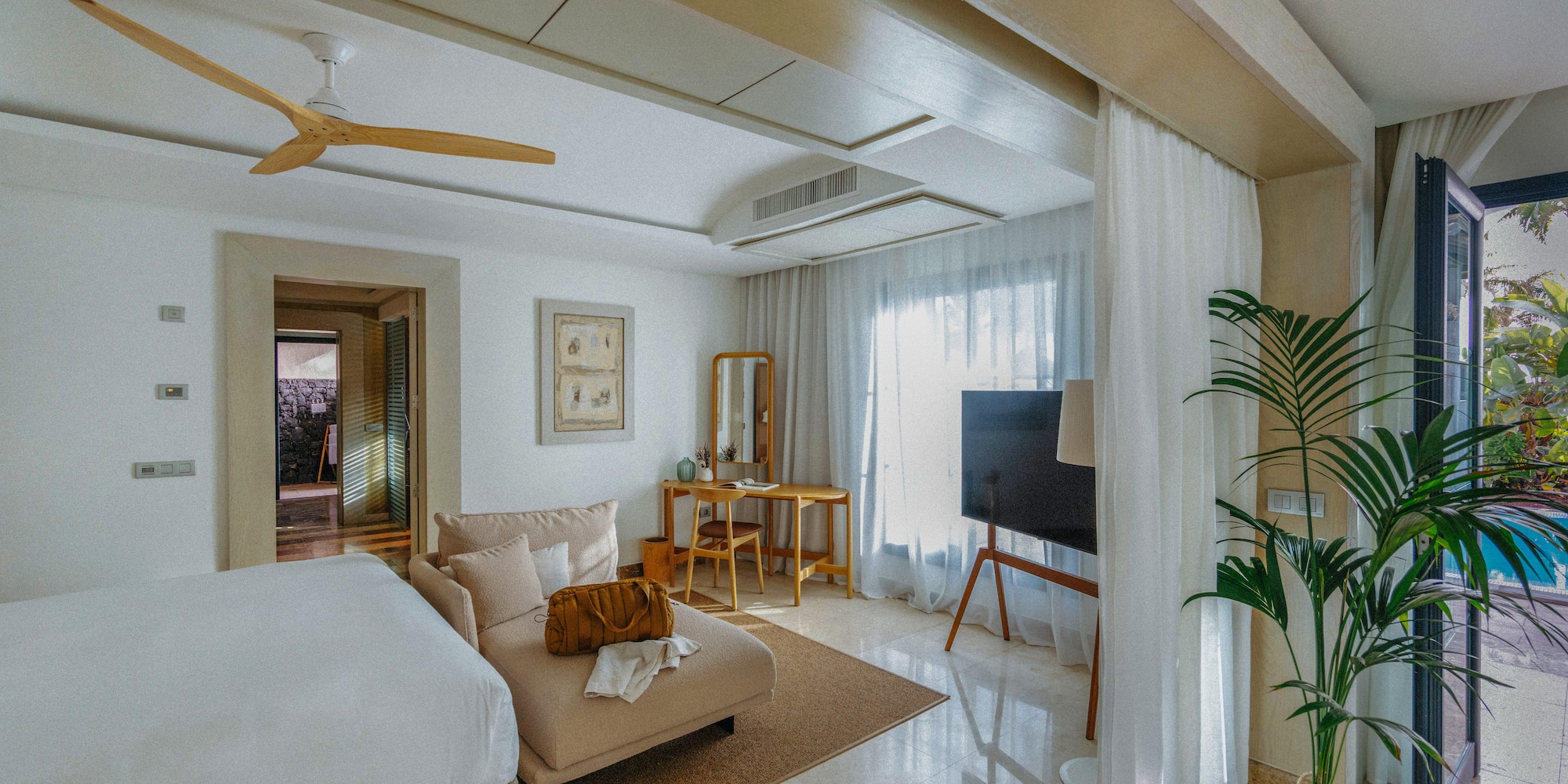 Modern bedroom with chaise lounge, wood desk, ceiling fan, and outdoor pool.