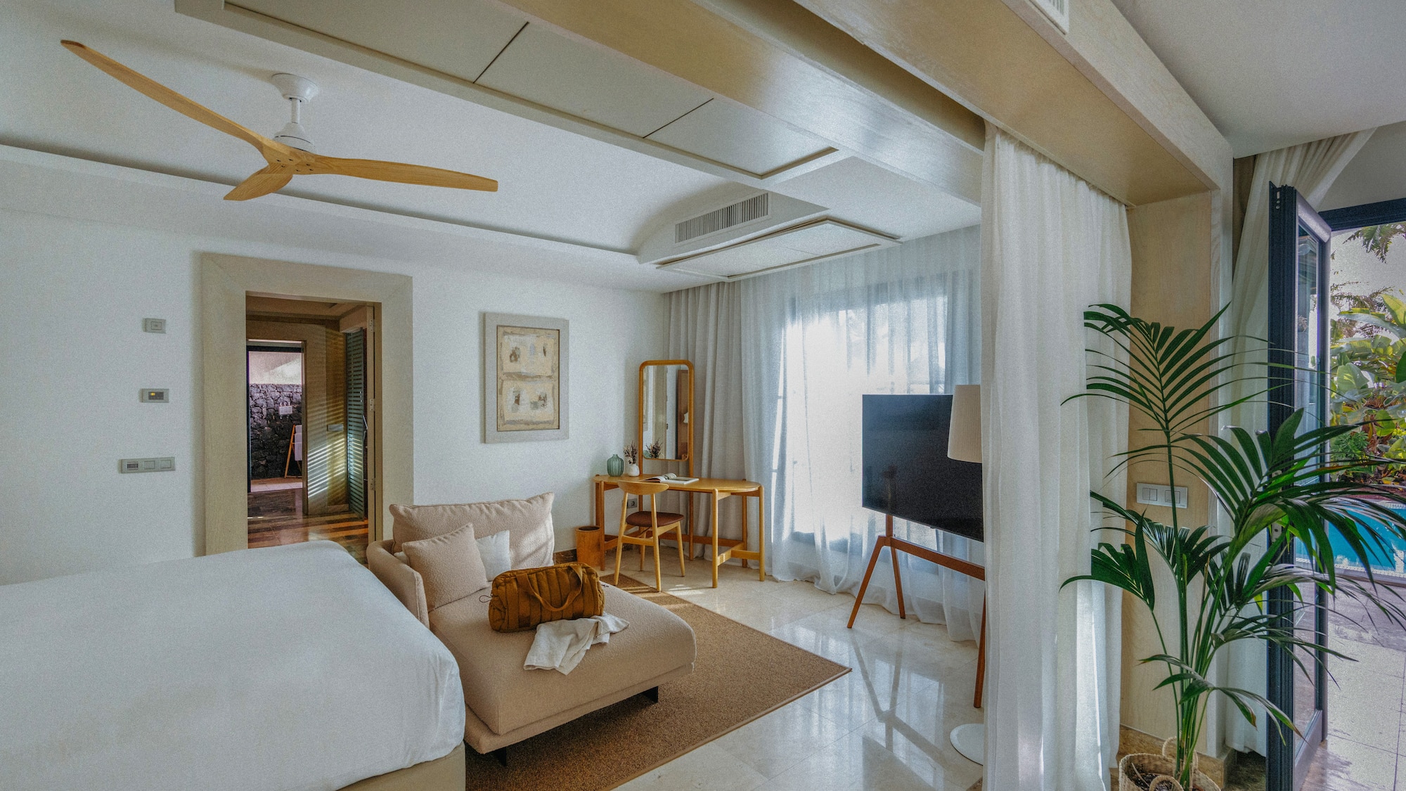 Modern bedroom with chaise lounge, wood desk, ceiling fan, and outdoor pool.
