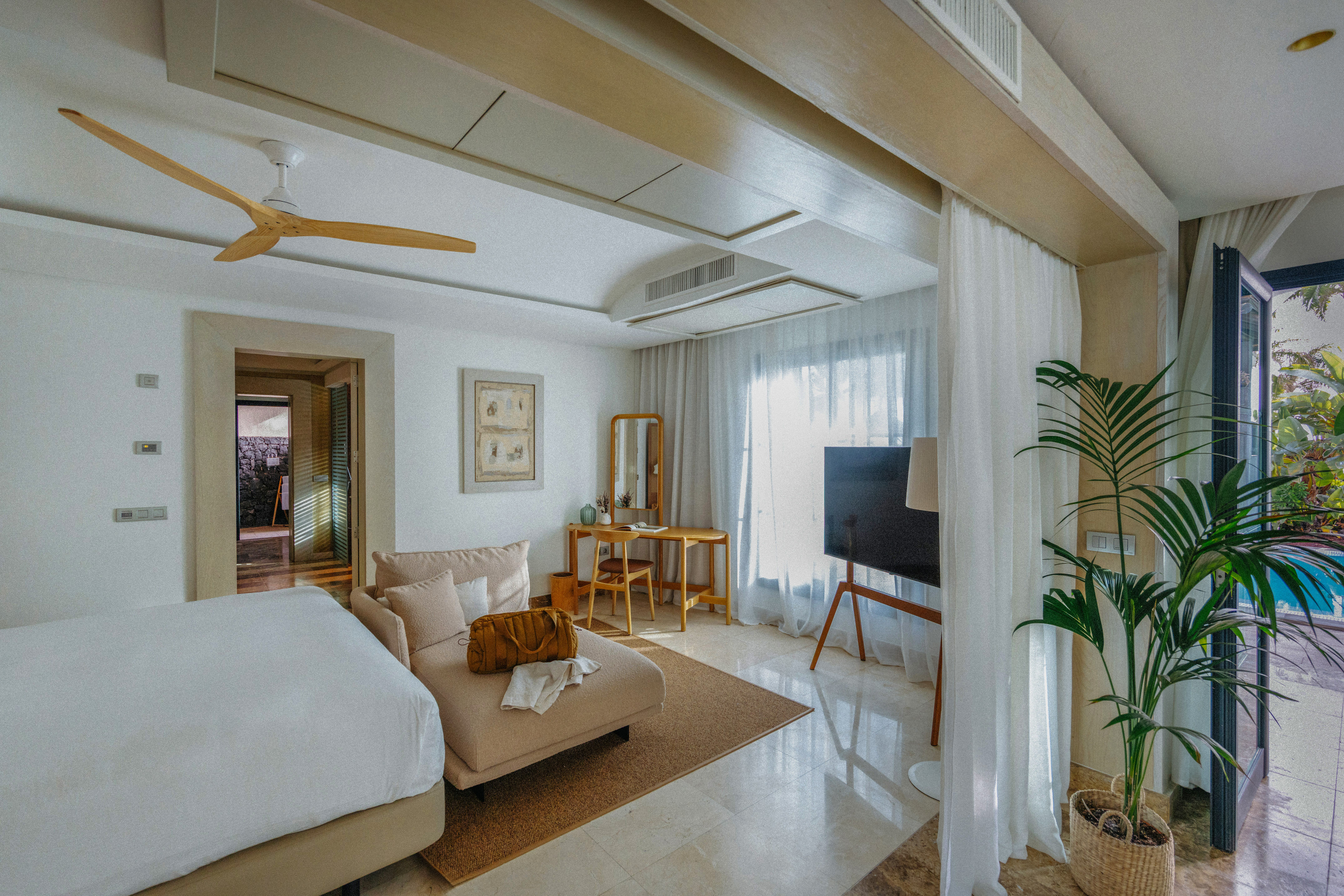 Modern bedroom with chaise lounge, wood desk, ceiling fan, and outdoor pool.