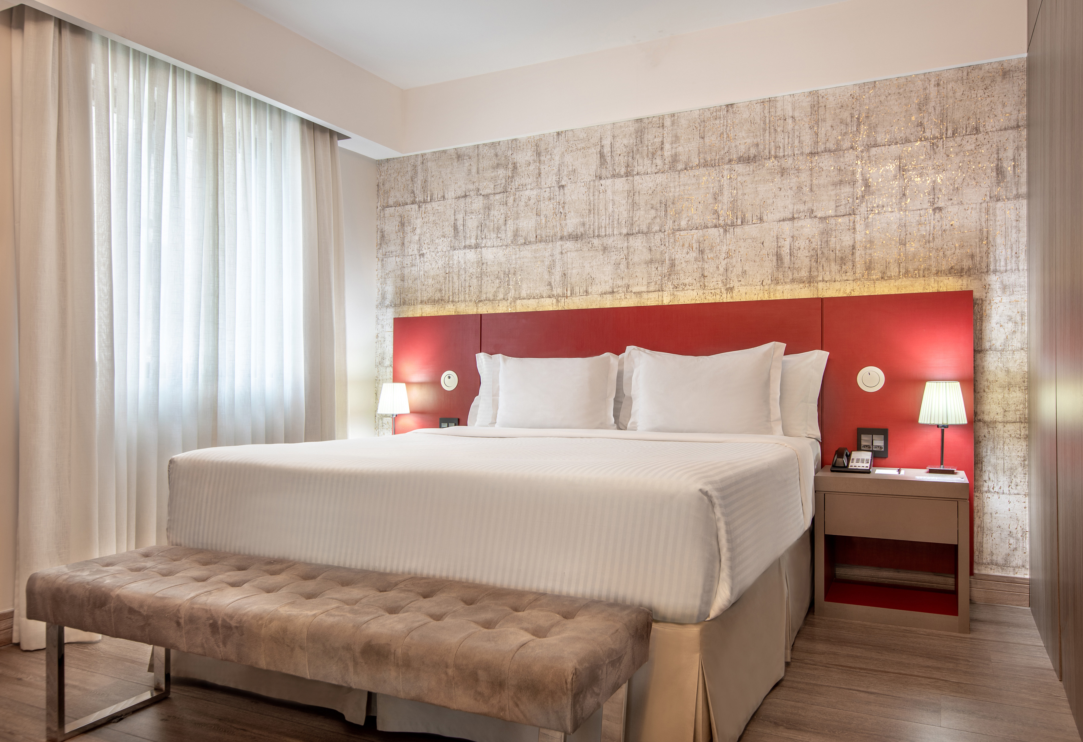 Luxurious hotel room with king bed, red headboard, and textured wall.