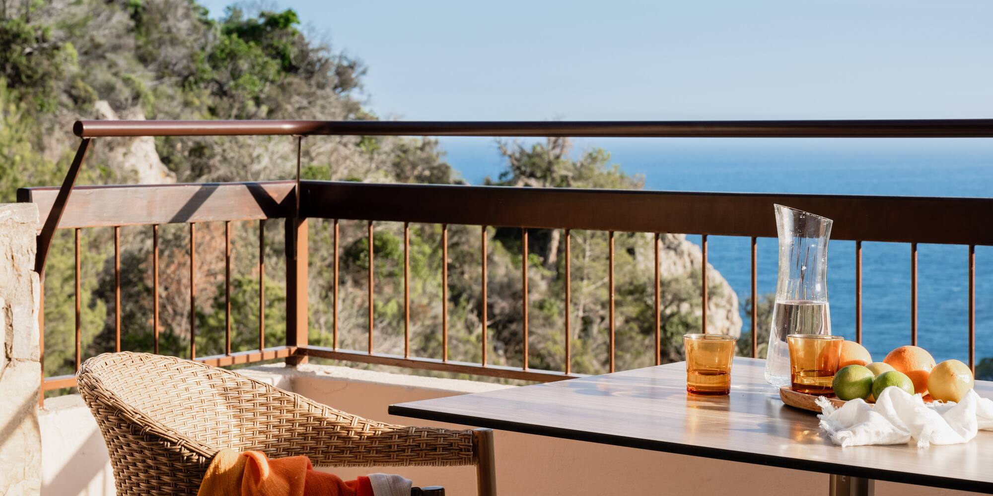 a table with glasses and a chair on a balcony overlooking the ocean
