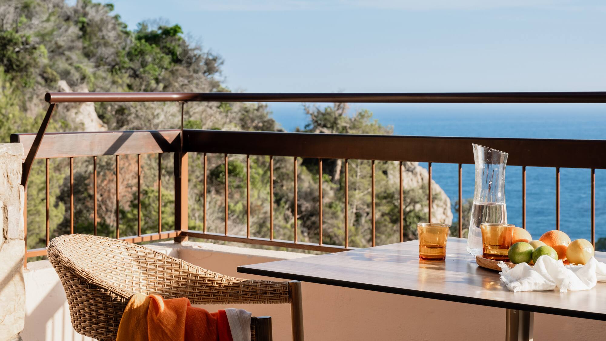 a table with glasses and a chair on a balcony overlooking the ocean