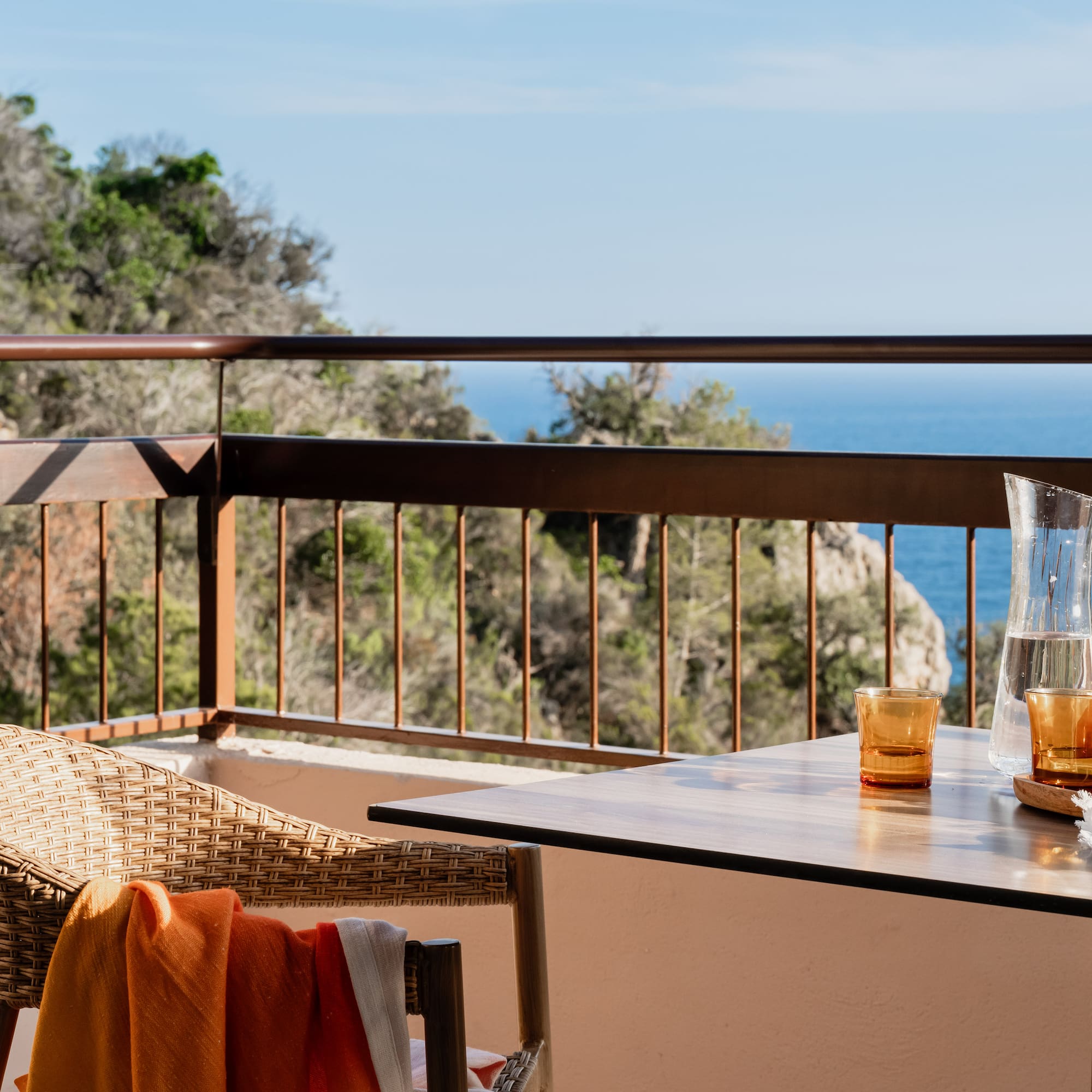 a table with glasses and a chair on a balcony overlooking the ocean