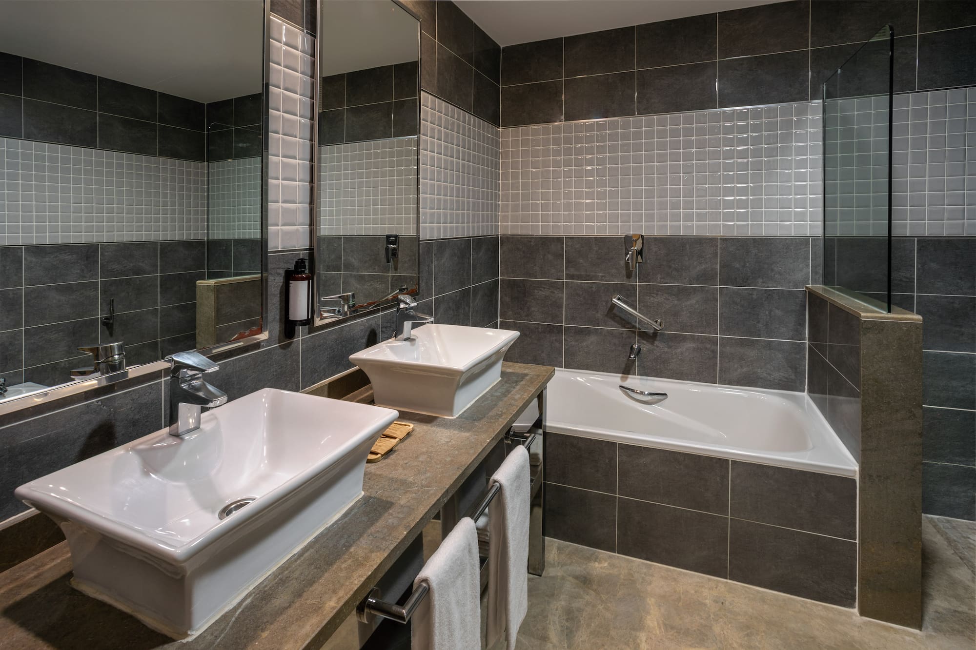Stylish grey tiled bathroom with double sinks and bathtub.