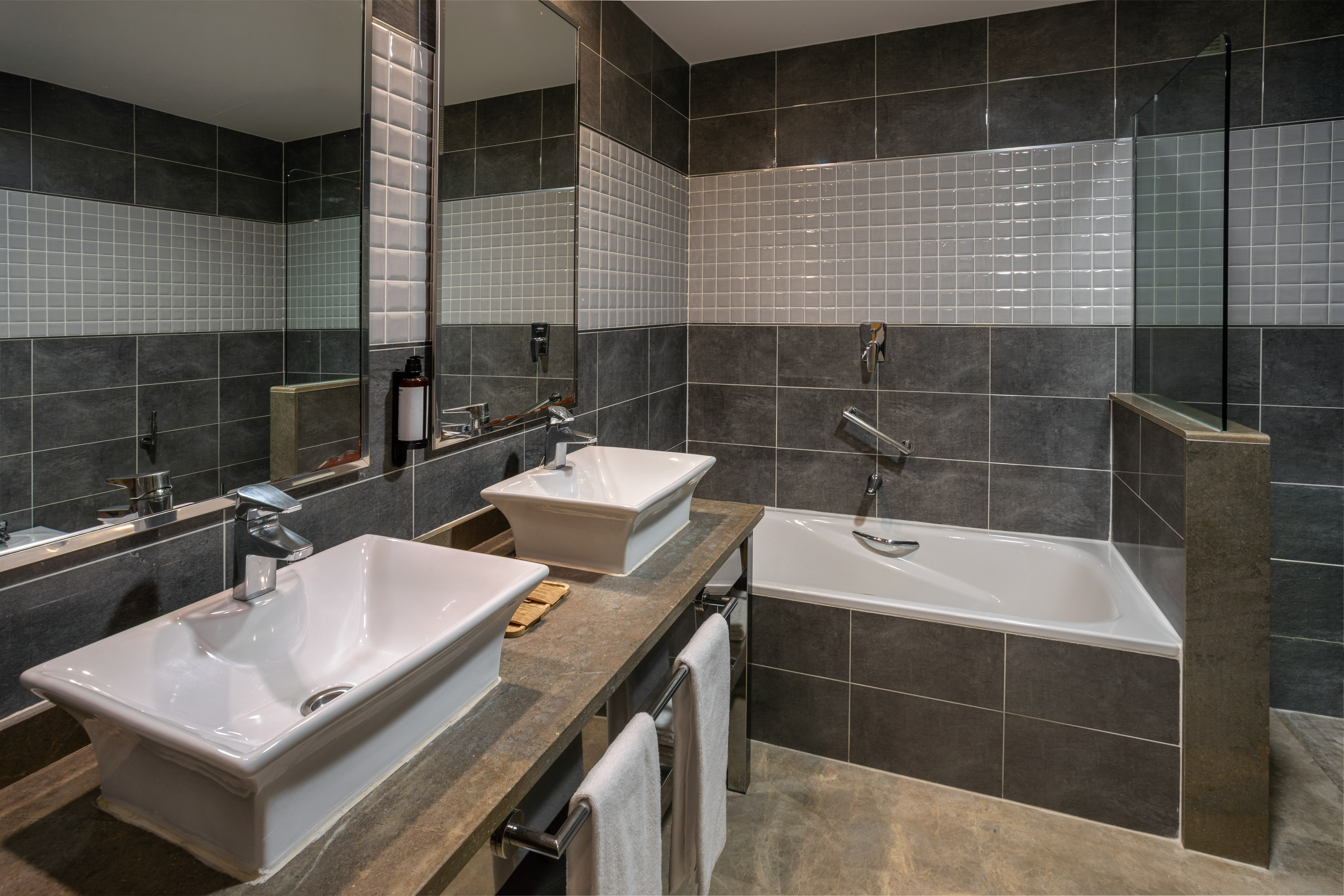 Stylish grey tiled bathroom with double sinks and bathtub.
