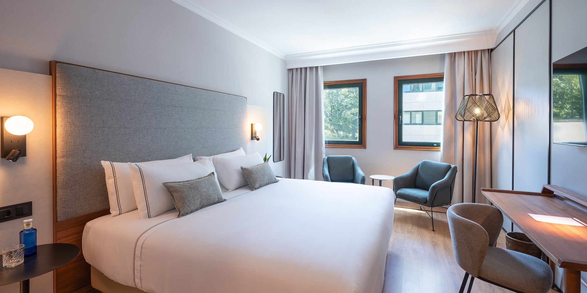 Habitación de hotel moderna con cama doble, sillones, escritorio y ventanal.