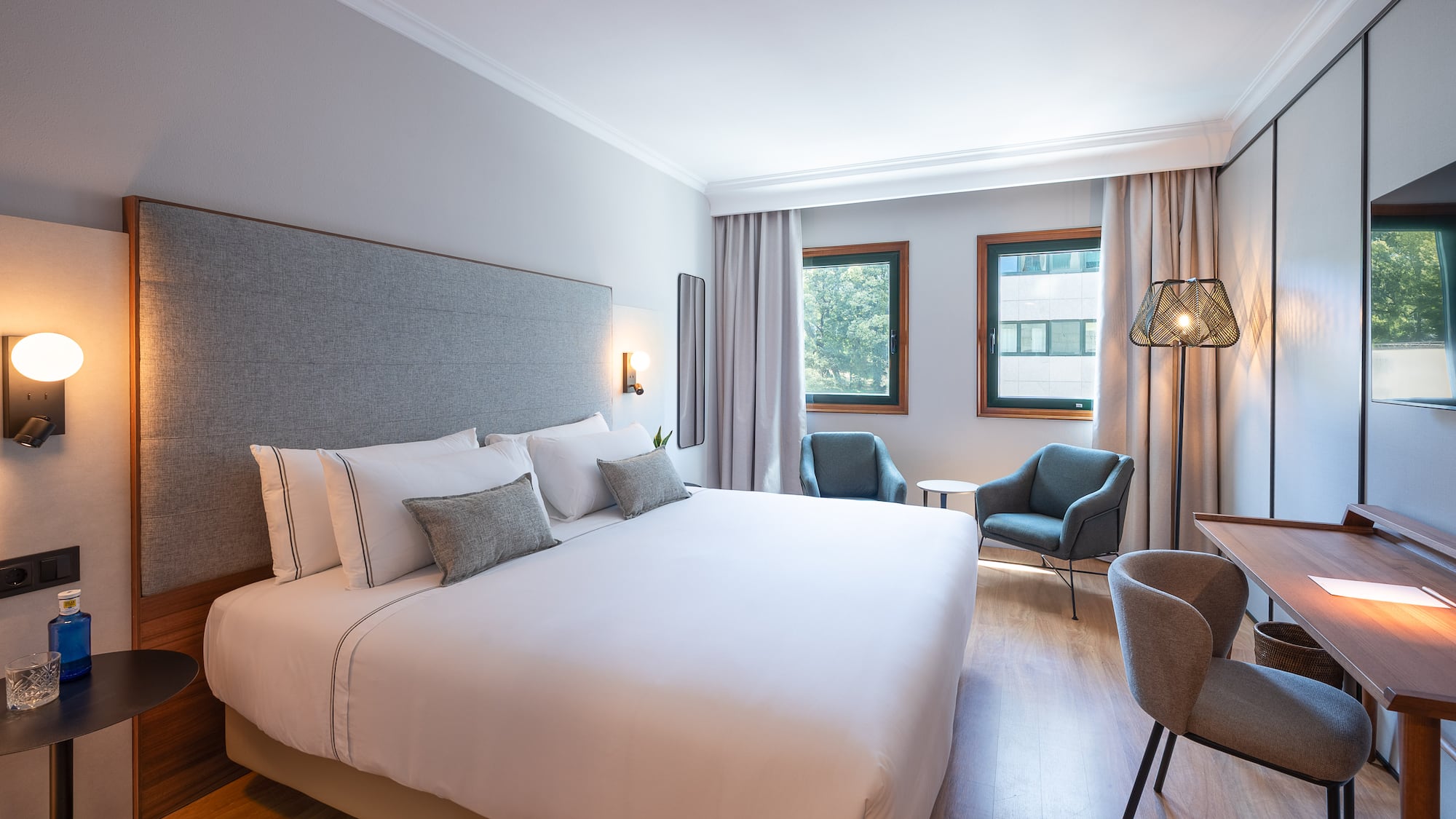 Spacious hotel room with large bed, plush seating, desk, and natural light.