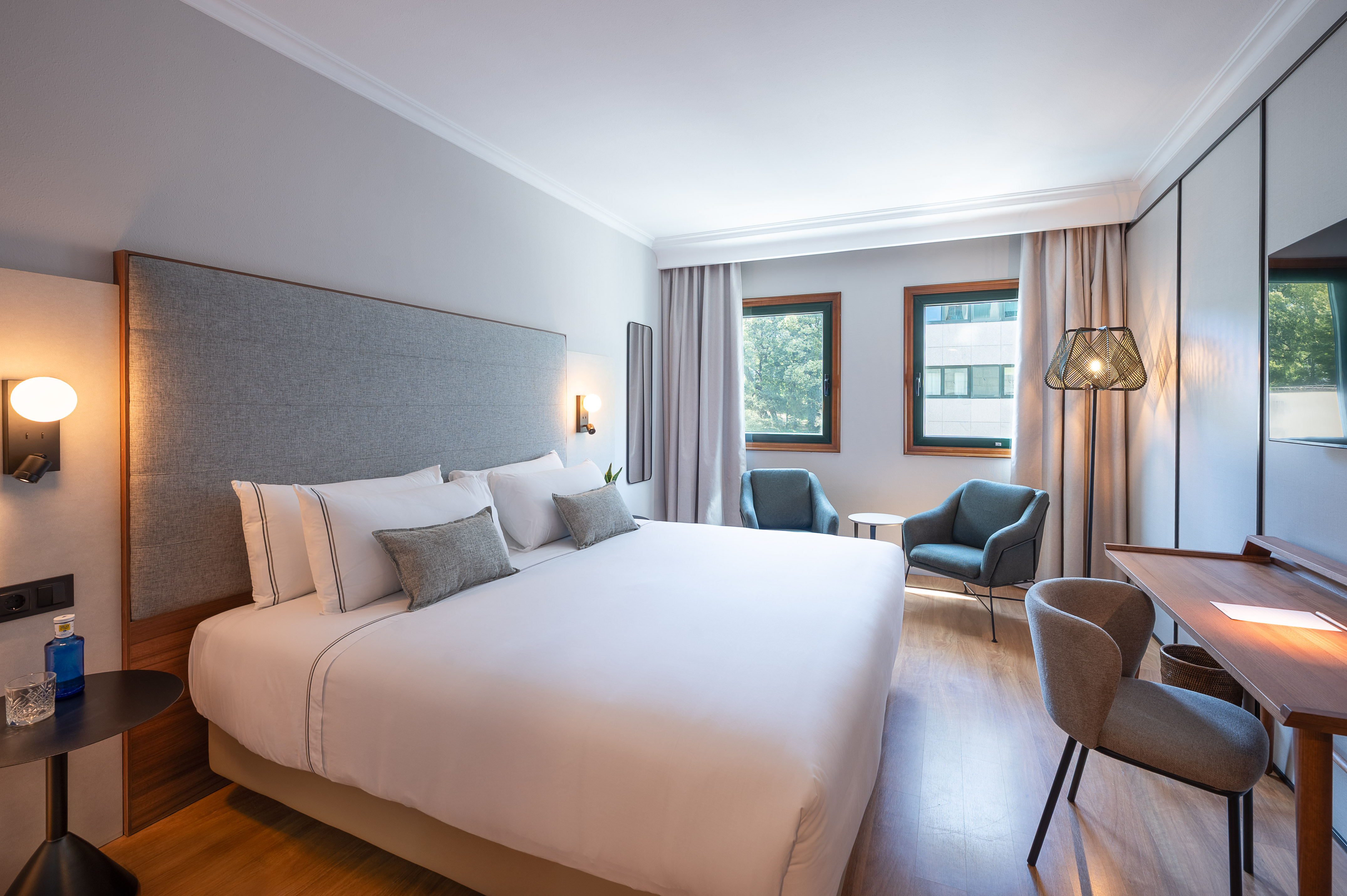 Dormitorio de hotel, cama king-size, sillones, escritorio y ventanas.