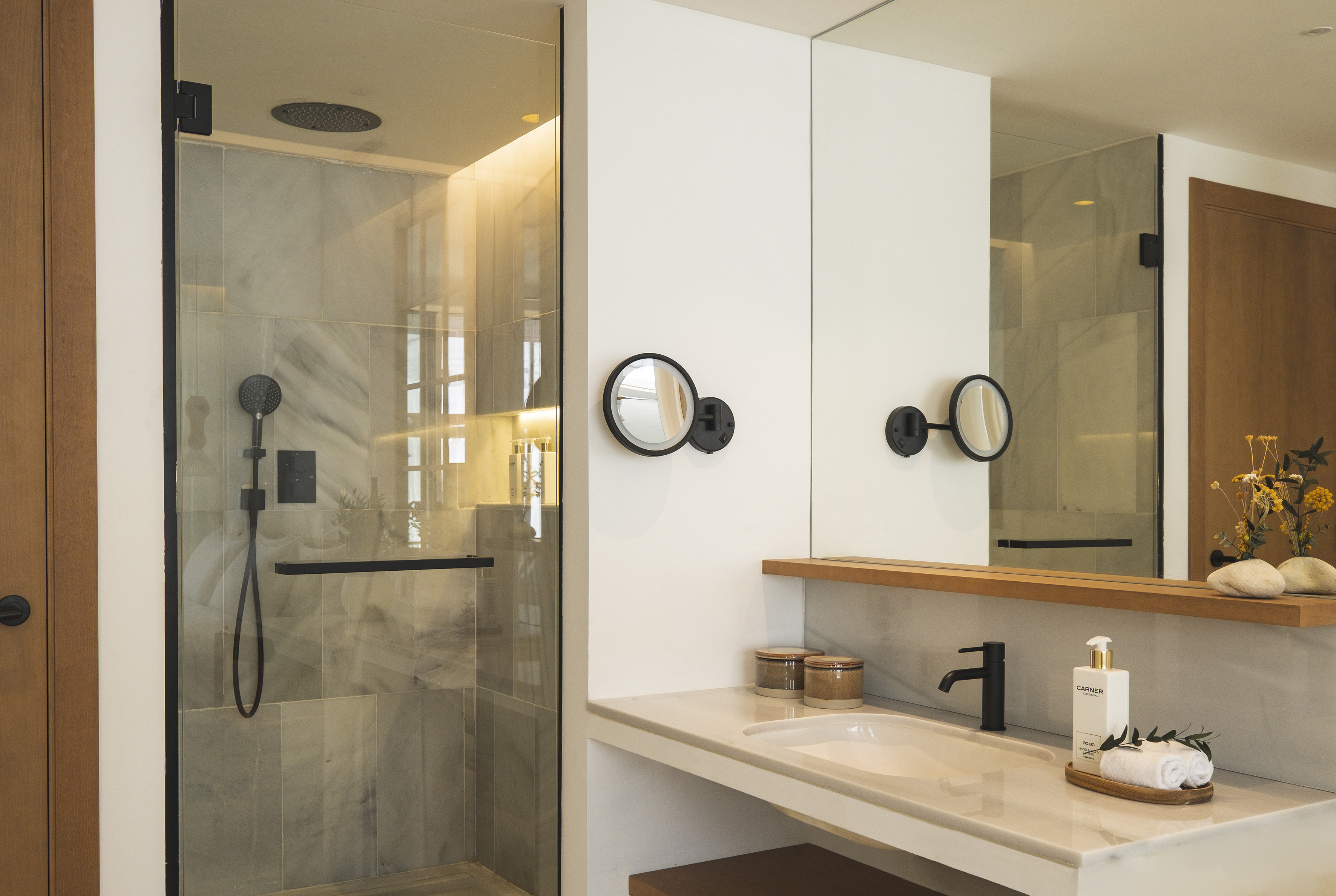 Modern bathroom with glass shower, marble vanity, black faucet, and wall mirrors.