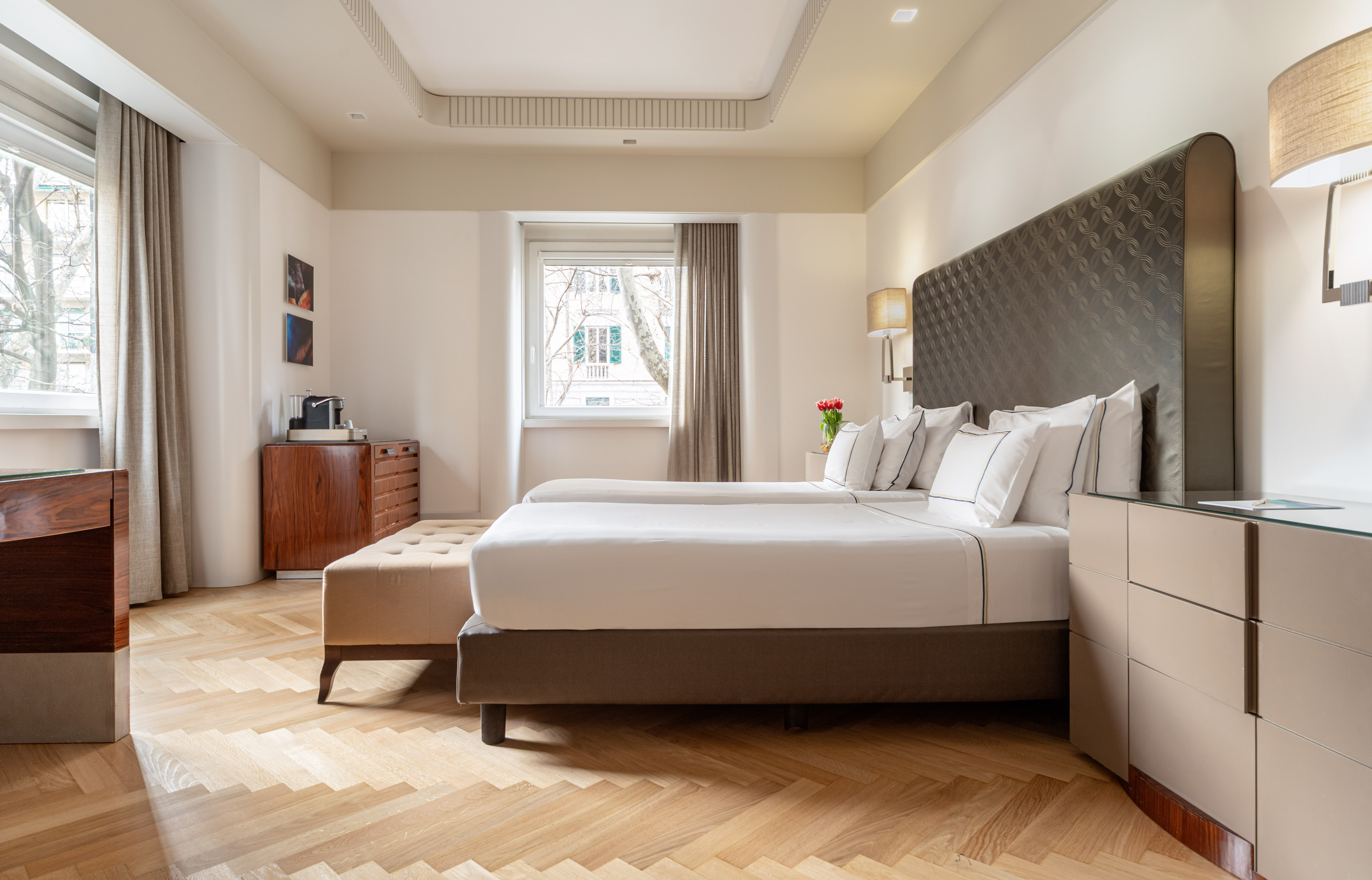 Modern hotel twin room with white bedding, dark headboard, and parquet floor.