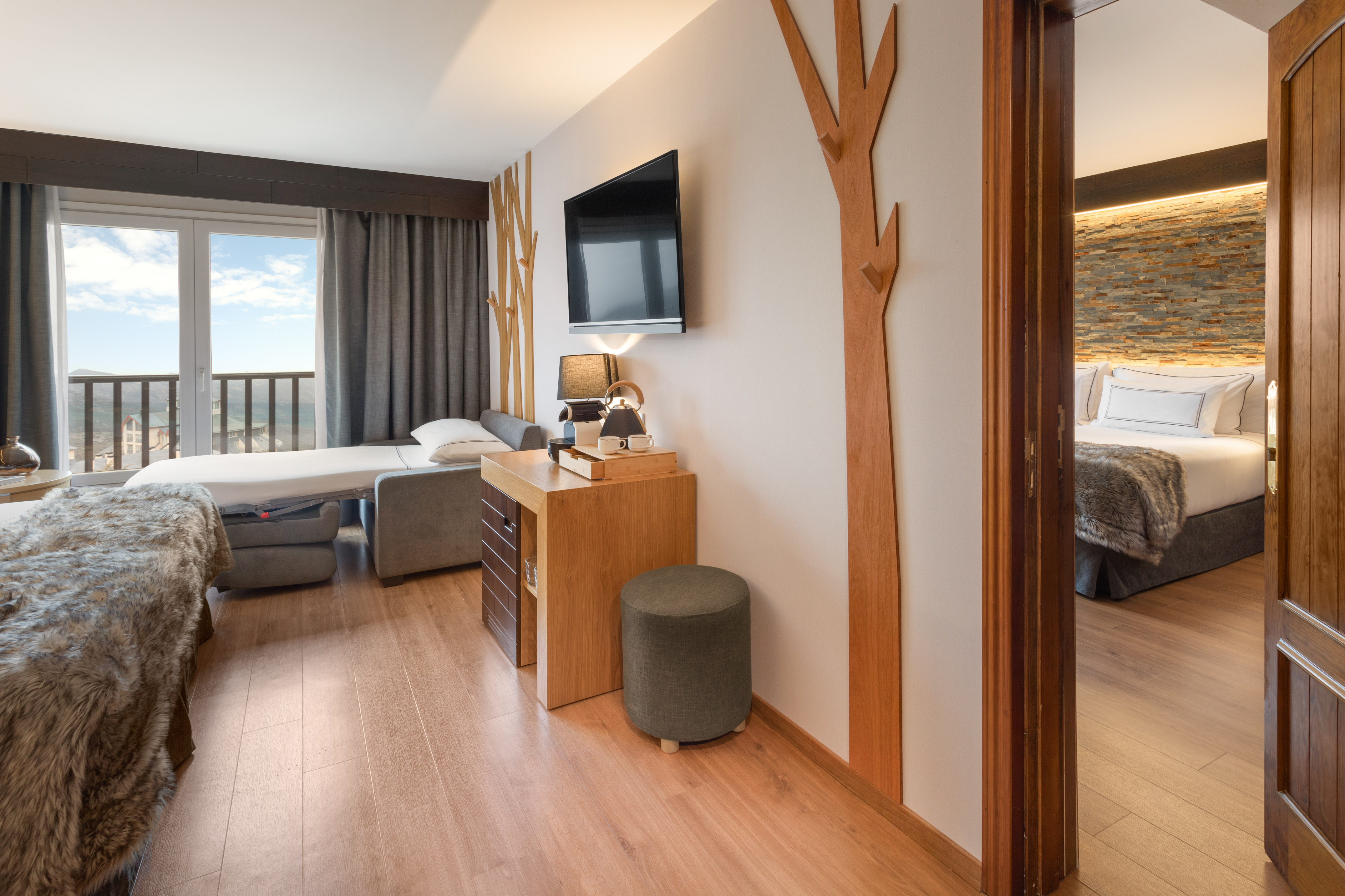 Hotel suite living area with sofa bed, balcony mountain view, TV, connecting bedroom.