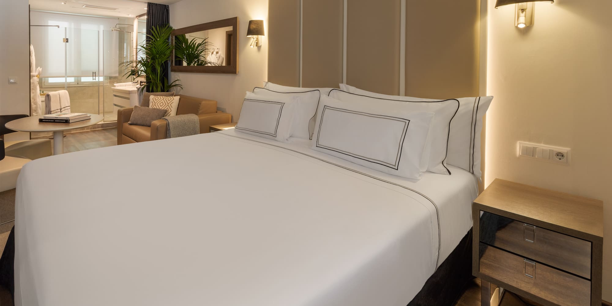 Elegant hotel room featuring a large bed, seating area, and open-plan bath.
