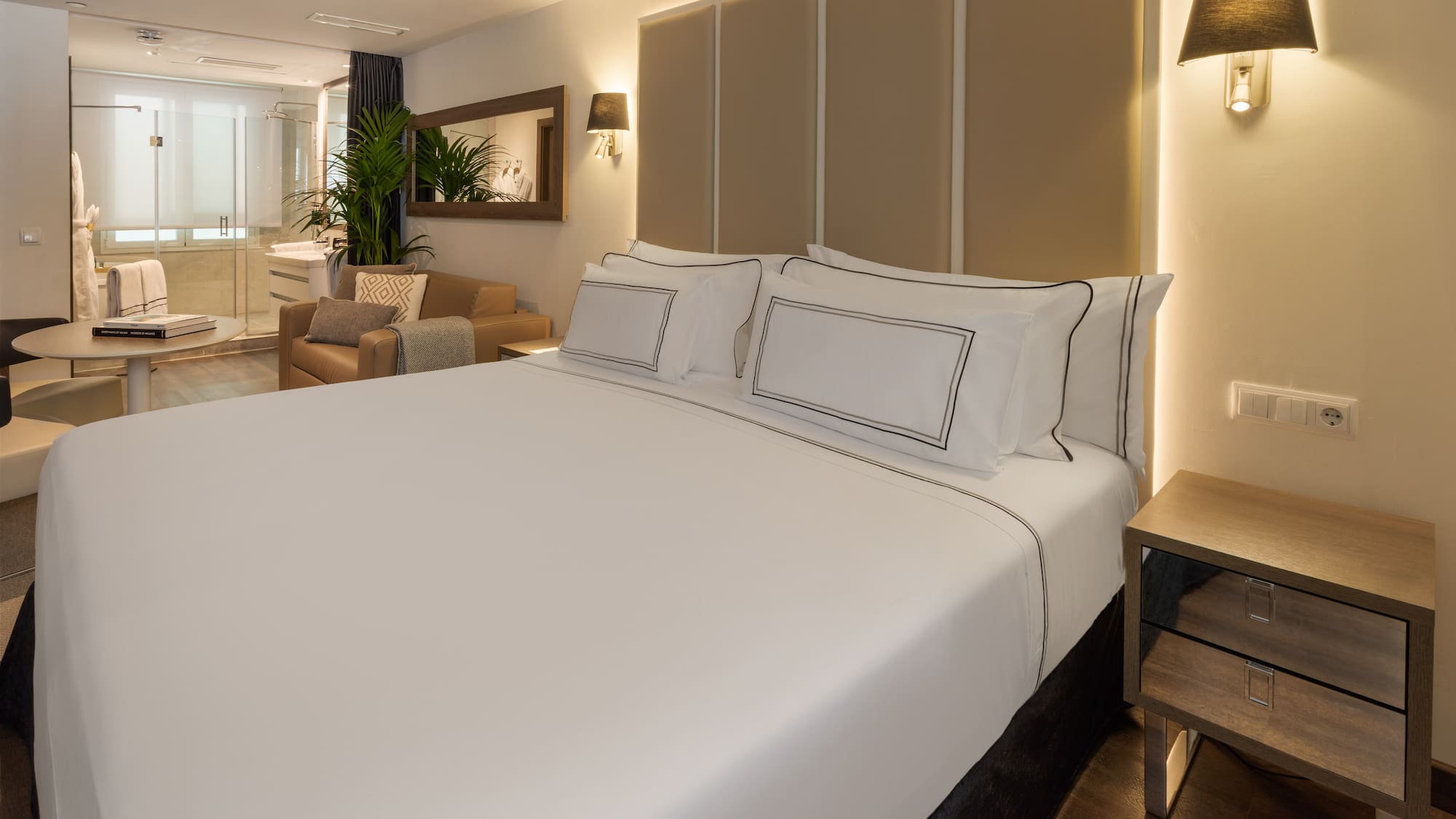 Modern hotel suite with large bed, sitting area, and bright open bathroom.