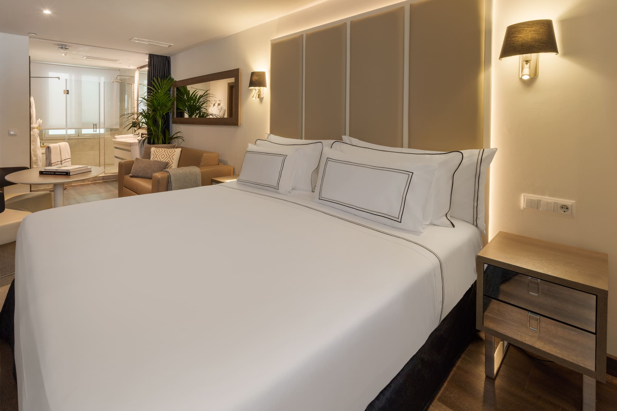 Modern hotel suite with large bed, sitting area, and bright open bathroom.