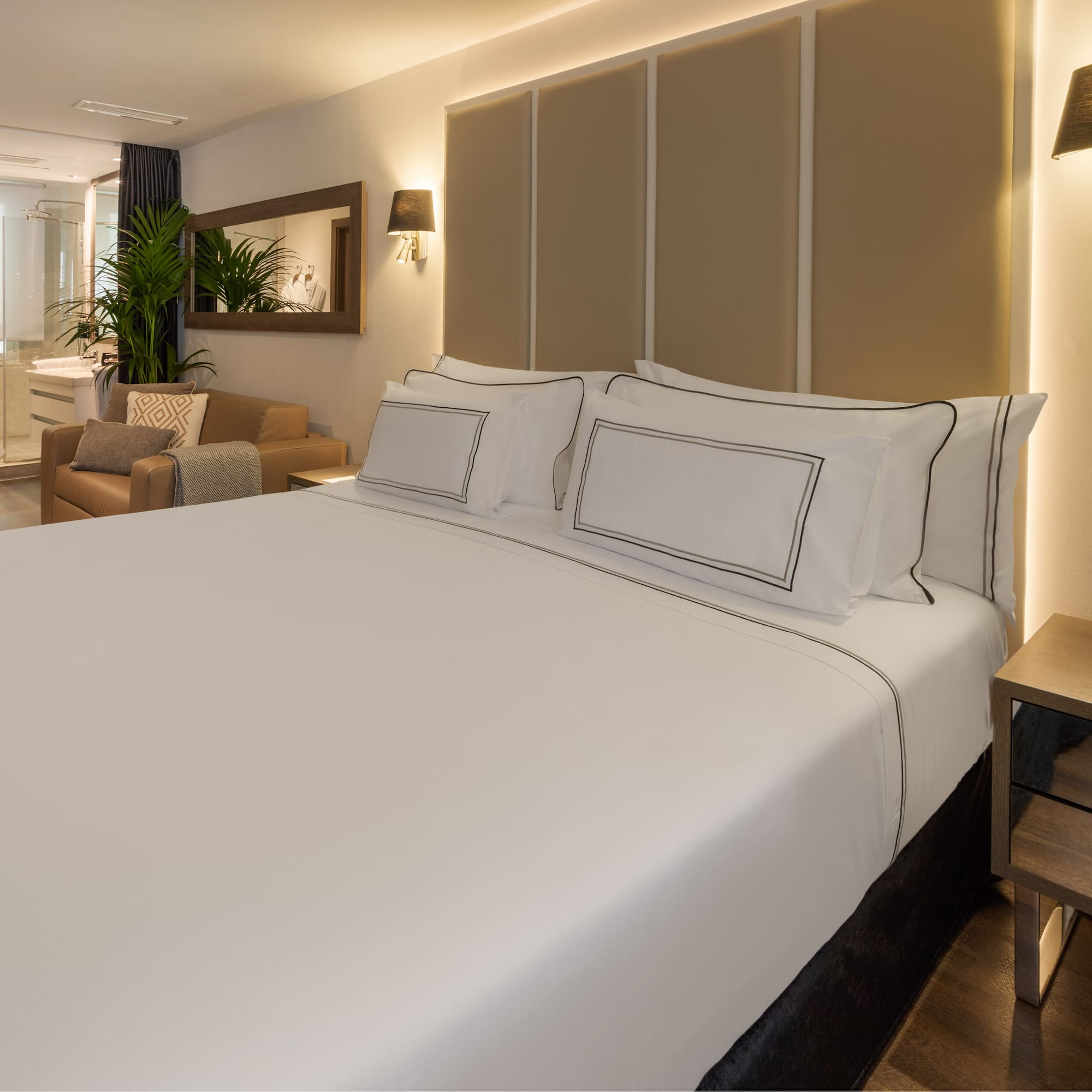 Modern hotel suite with large bed, sitting area, and bright open bathroom.