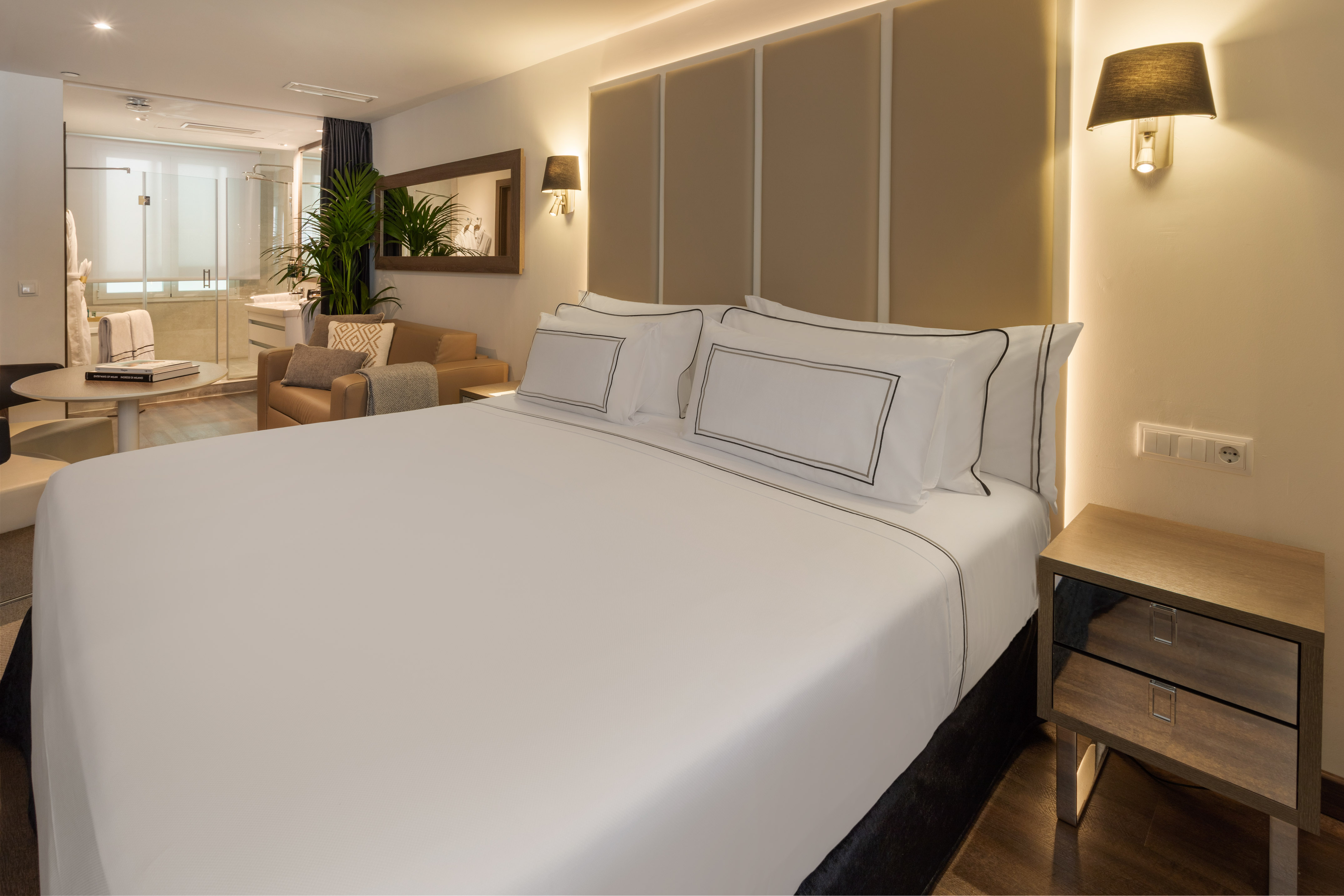 Modern hotel suite with large bed, sitting area, and bright open bathroom.