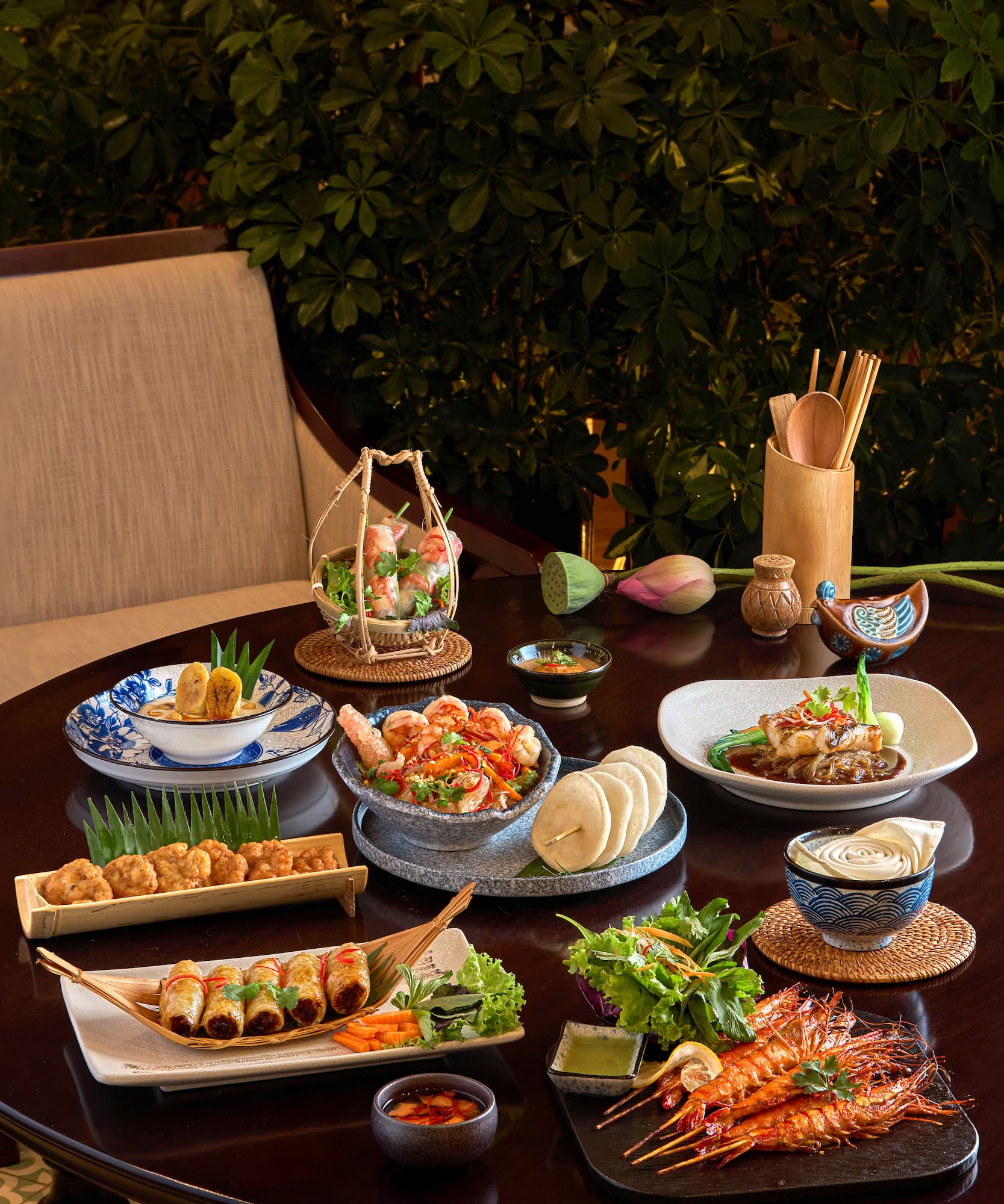 Vietnamese dishes on dining table: spring rolls, grilled shrimp, fish, and salads.