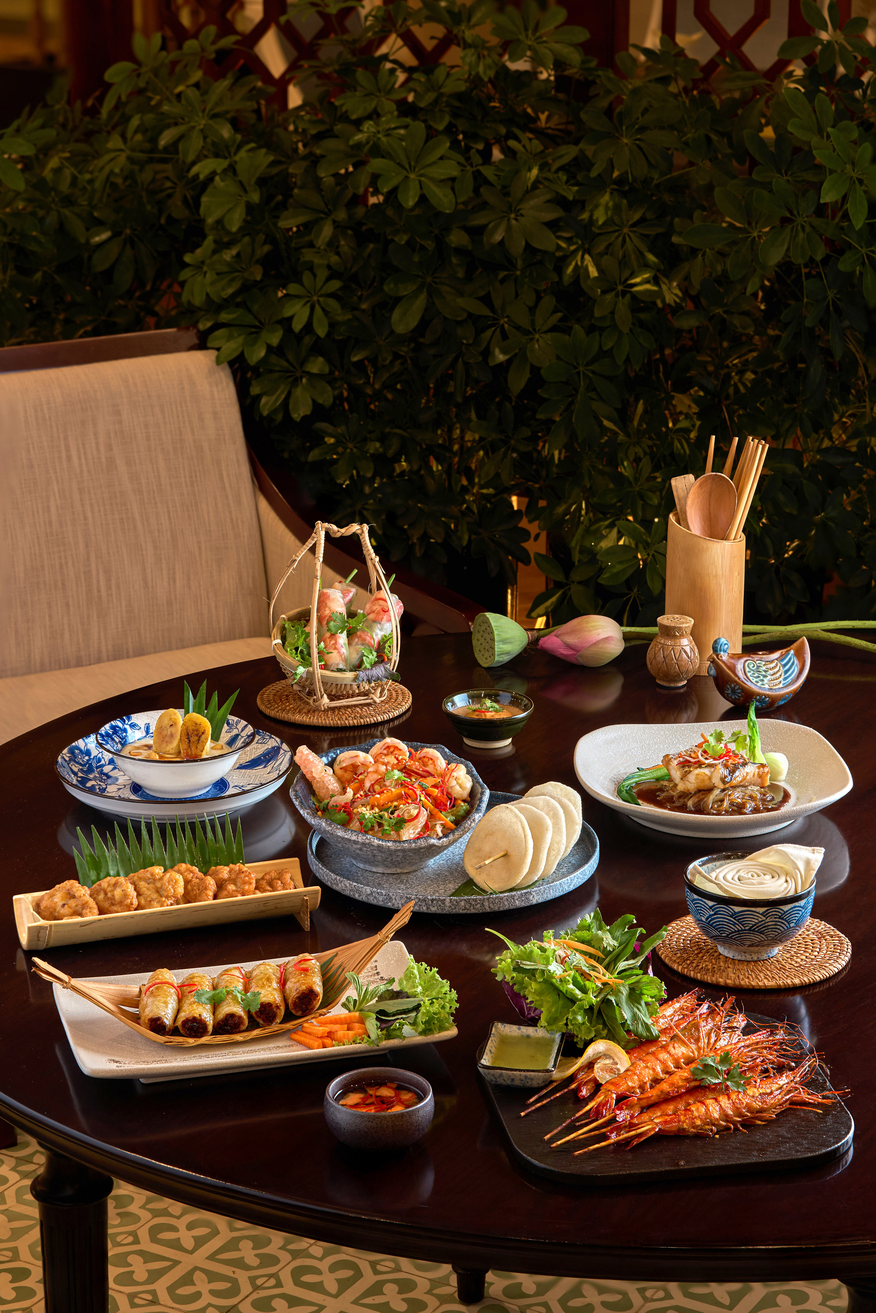 Vietnamese dishes on dining table: spring rolls, grilled shrimp, fish, and salads.