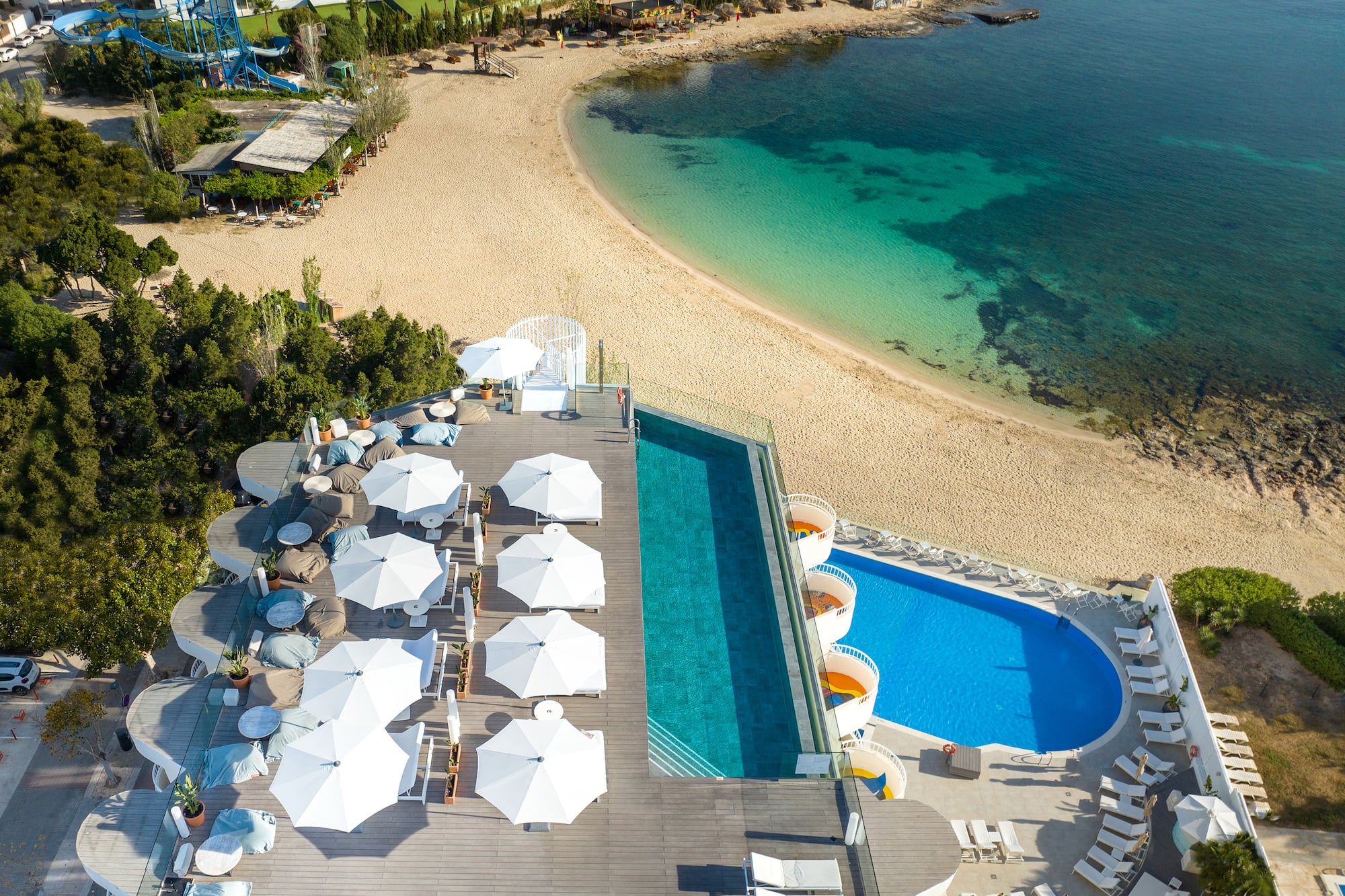 Resort aerial view: two pools, sandy beach, turquoise sea, white umbrellas.