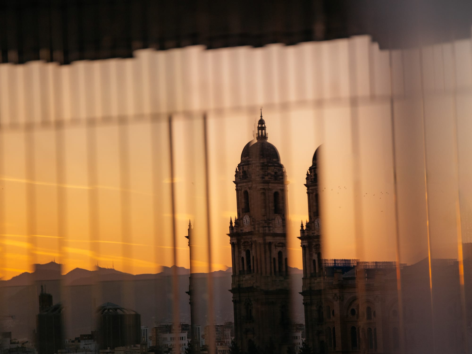 Málaga Cathedral tower and city skyline at sunset through reflective window.
