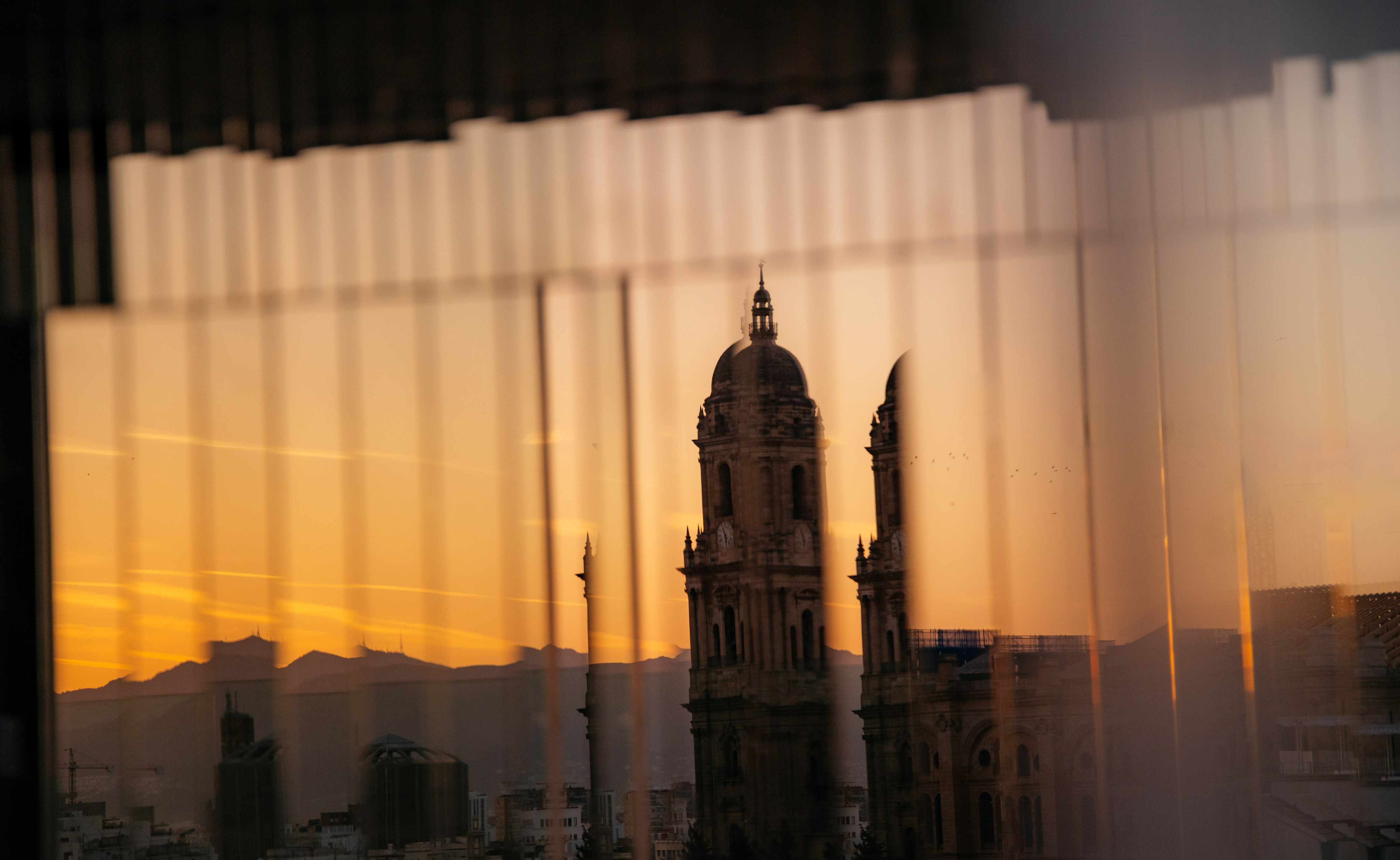 Málaga Cathedral tower and city skyline at sunset through reflective window.