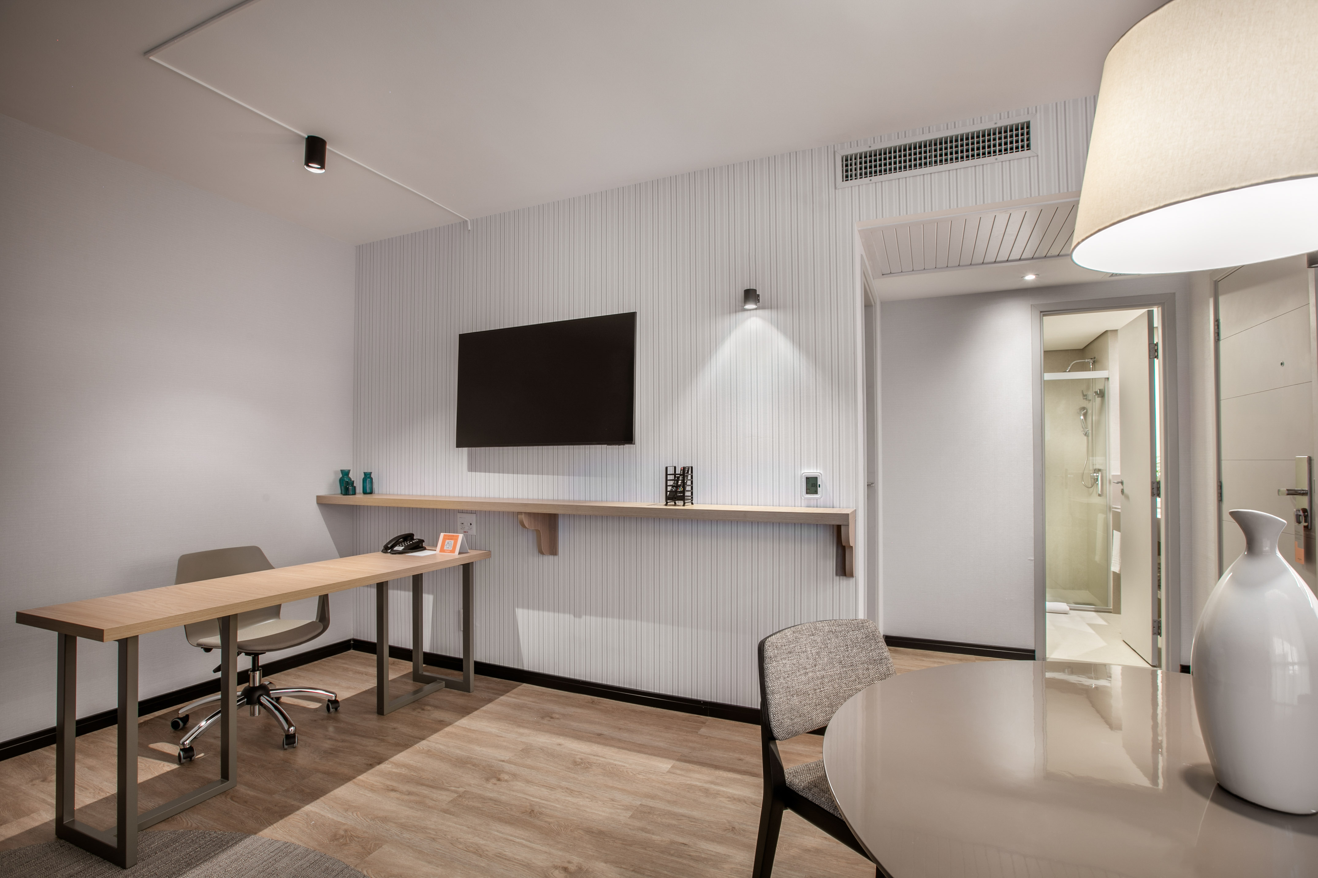 Modern hotel suite with a workspace, flat-screen TV, and light wood flooring.