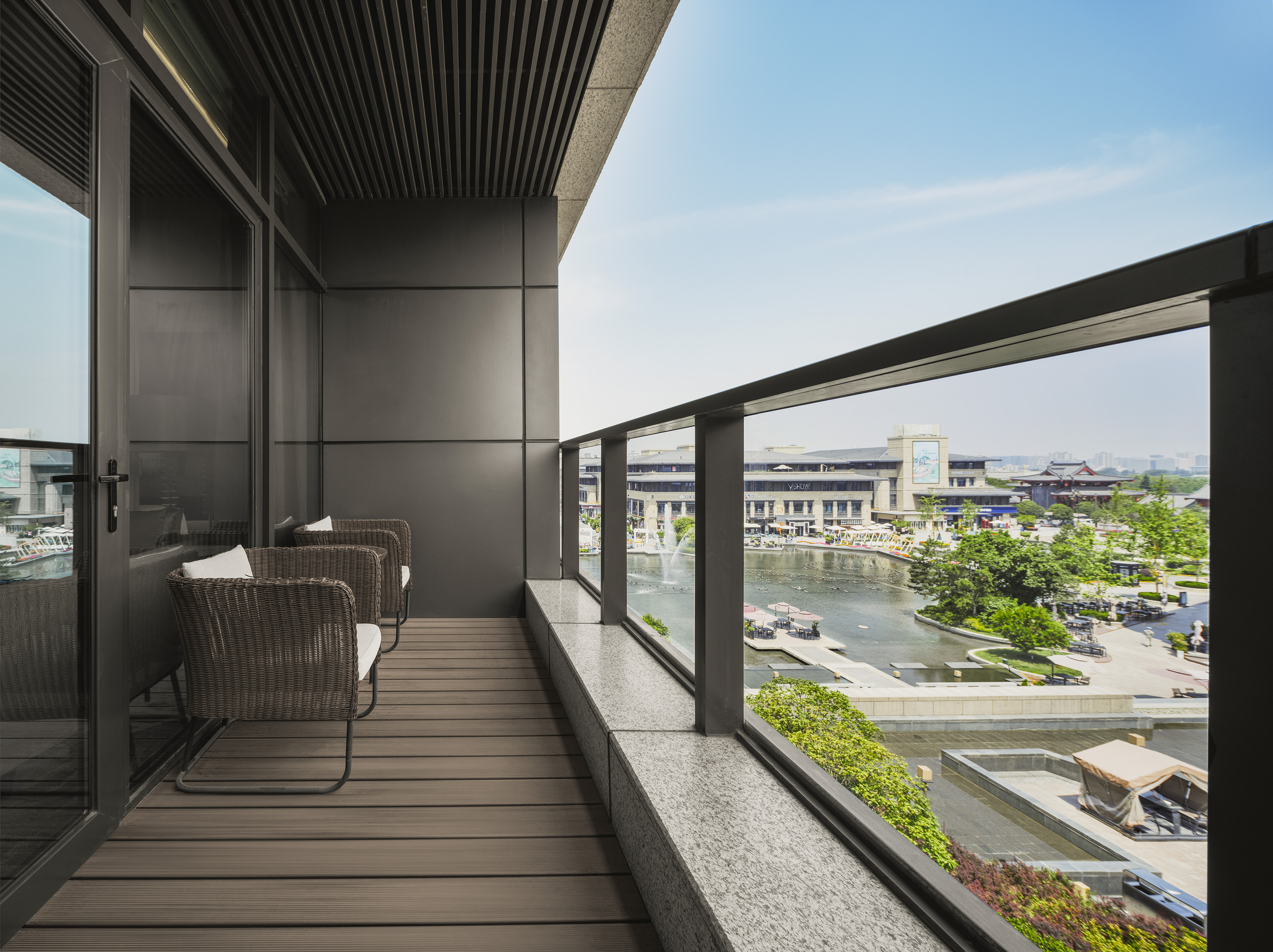 Modern balcony with two wicker chairs, glass railing, view of waterfront plaza.