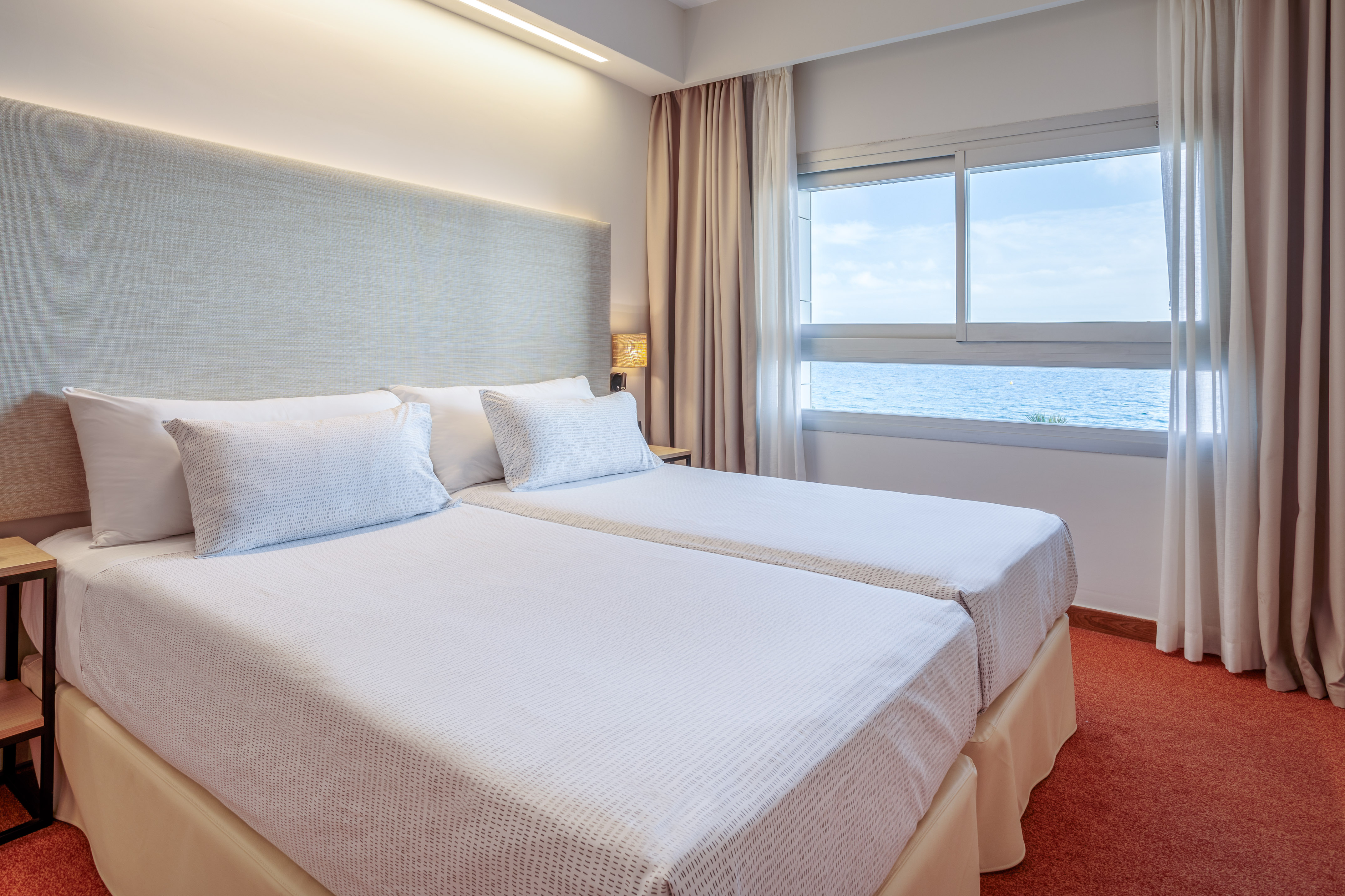 Hotel room with twin beds, white bedding, and large window overlooking the sea.