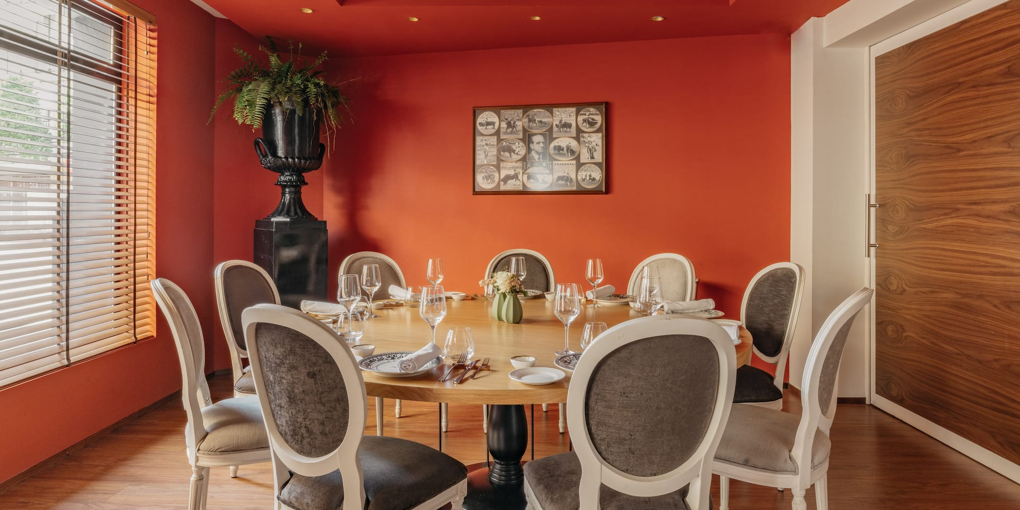 Comedor de restaurante con mesa redonda, paredes rojas, sillas y planta.