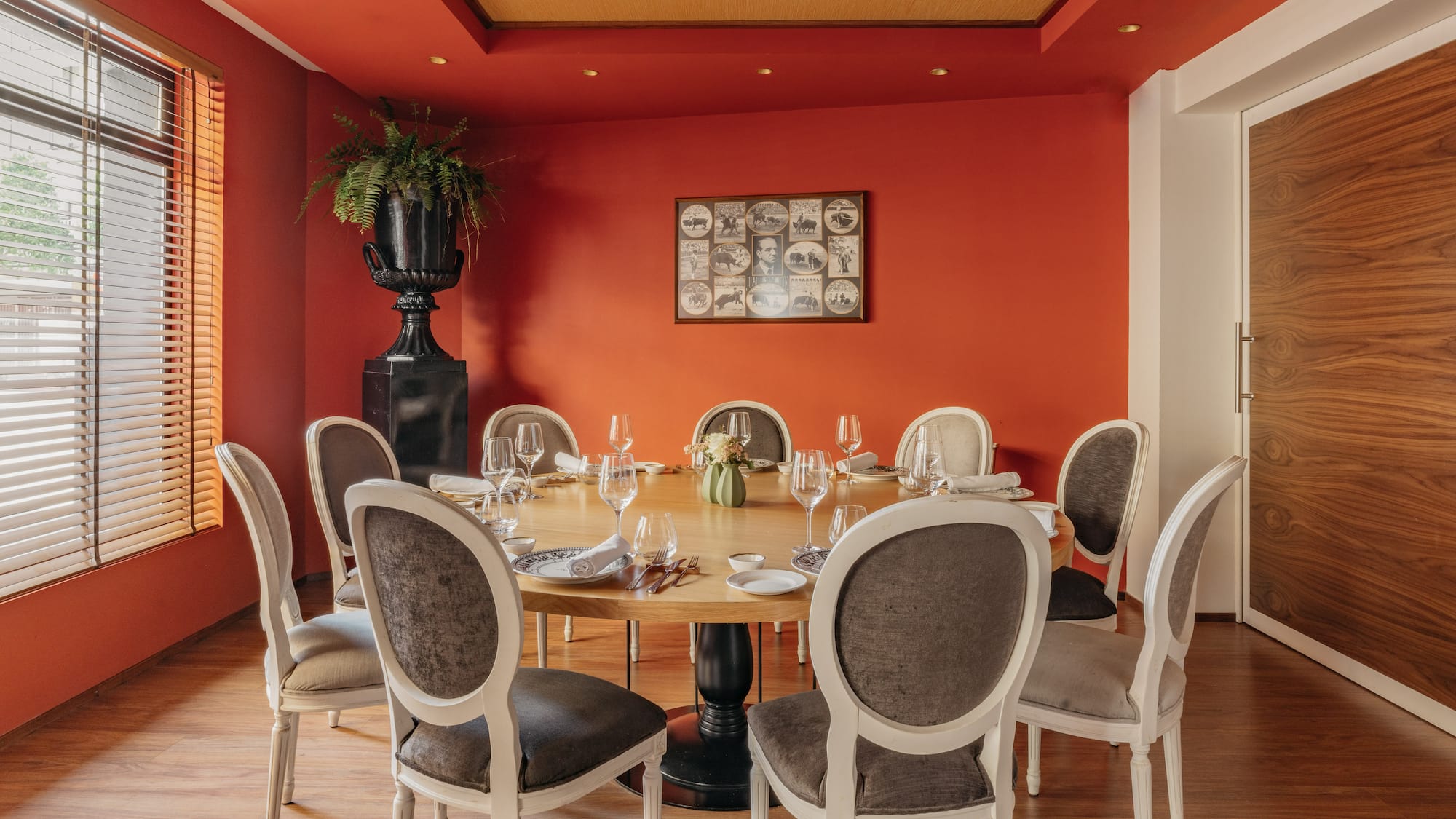 Comedor de restaurante con mesa redonda, paredes rojas, sillas y planta.