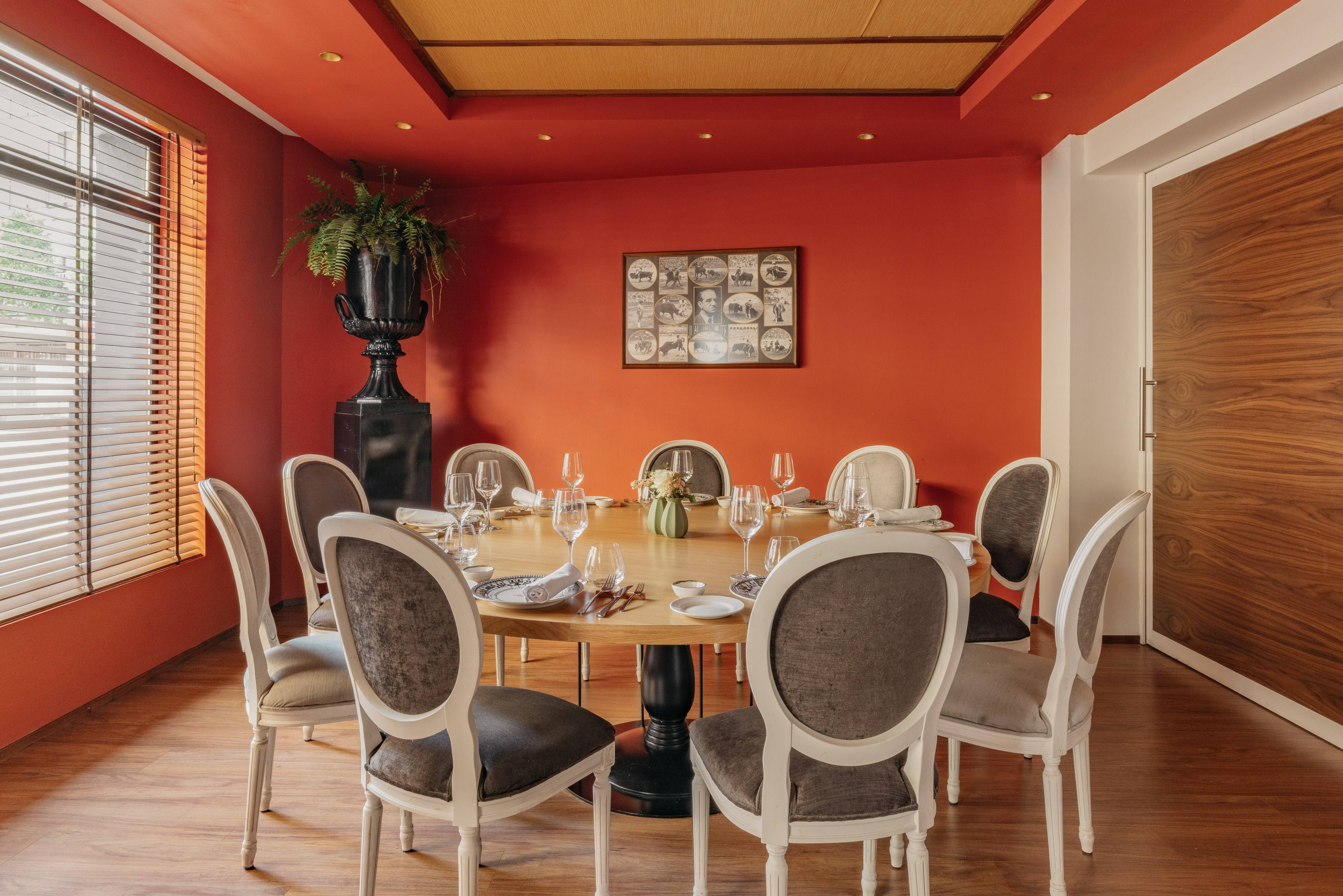 Comedor de restaurante con mesa redonda, paredes rojas, sillas y planta.