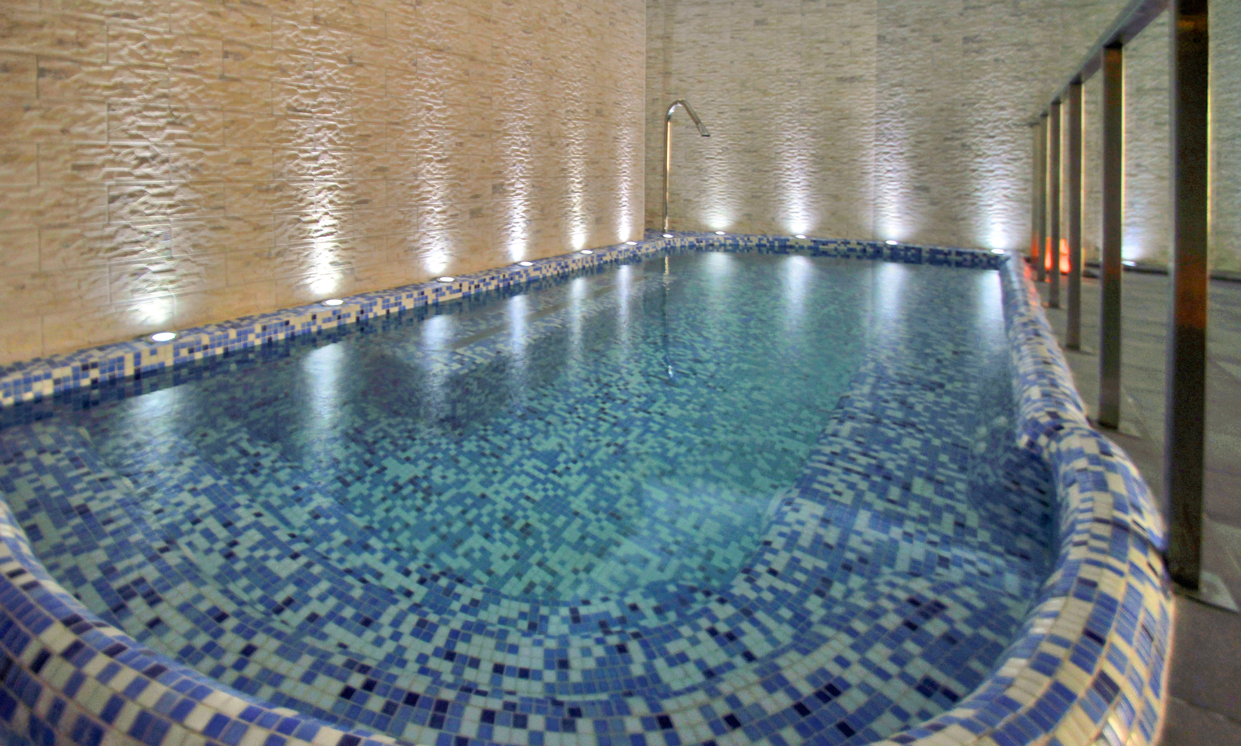 Indoor spa pool with blue mosaic tiles, textured wall, and accent lighting.