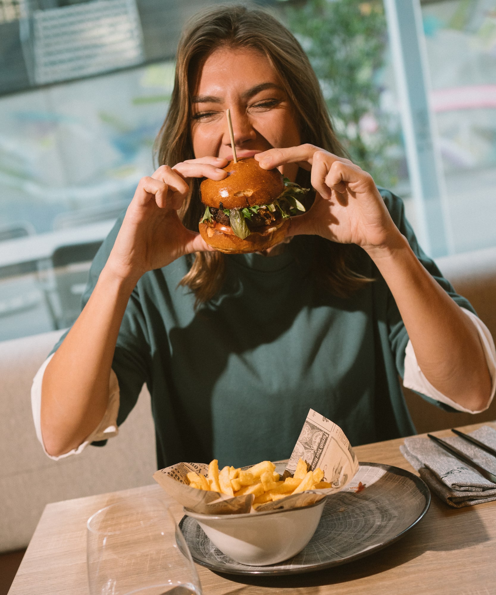 Woman happily eating a burger with french fries at a restaurant.