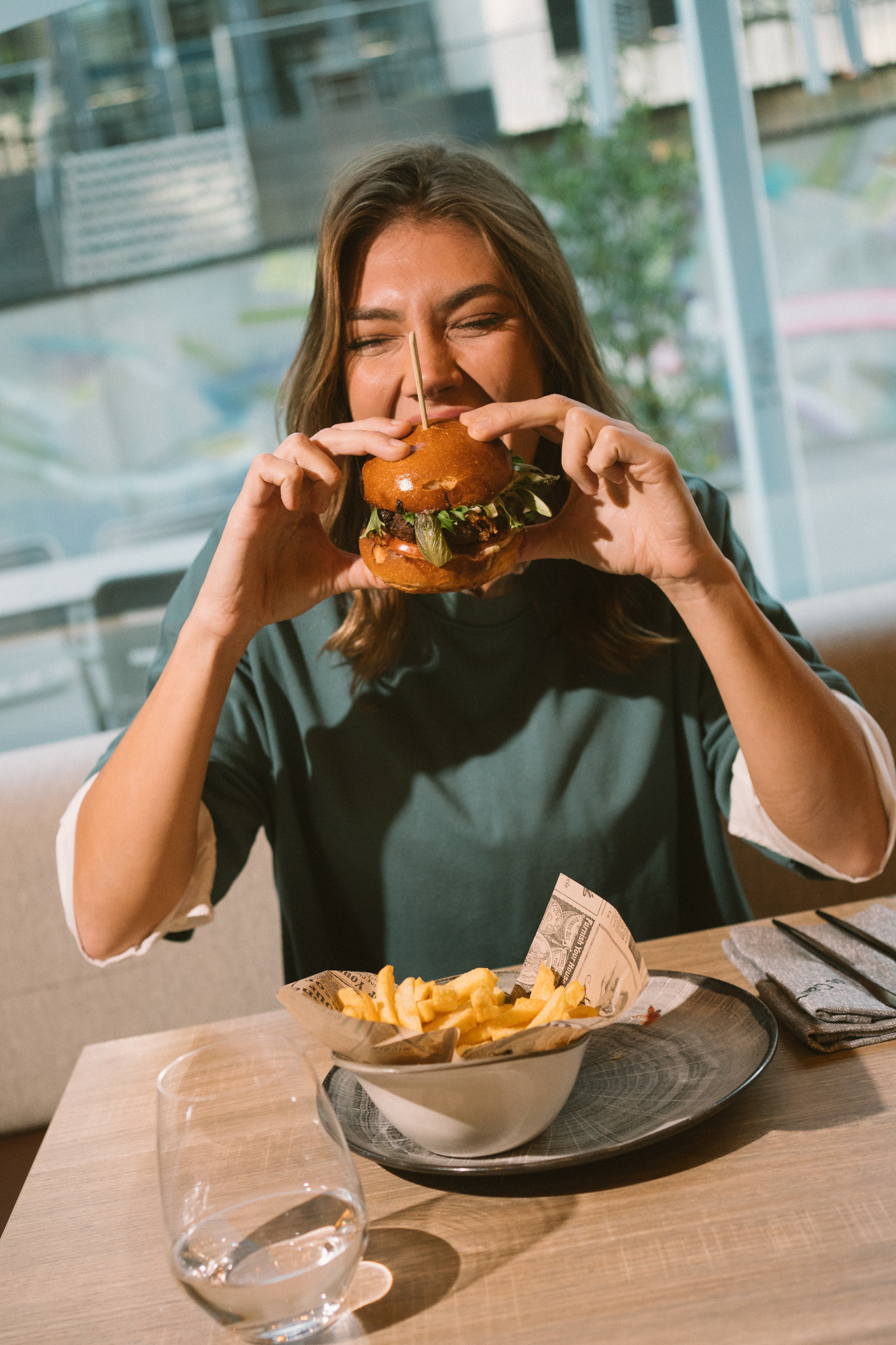 Woman happily eating a burger with french fries at a restaurant.